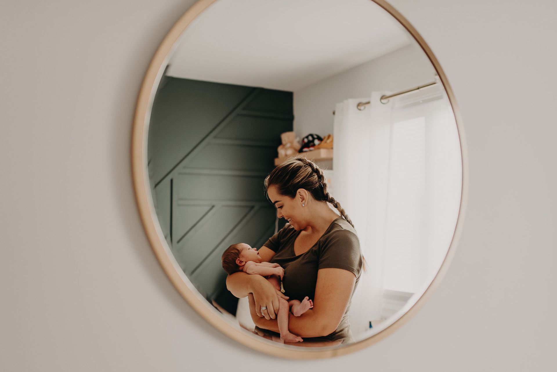 Reflection of a mother holding her newborn in front of a round wall mirror.