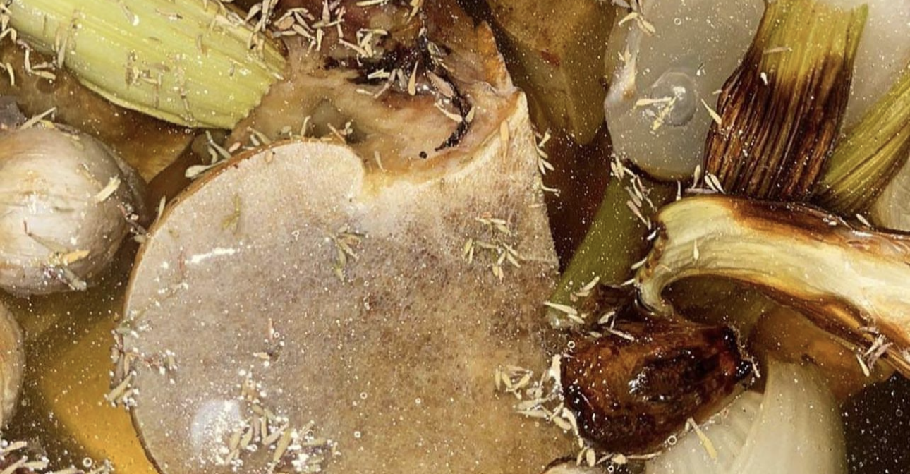 Bone broth simmering with herbs, onions, and vegetables for postpartum recovery.