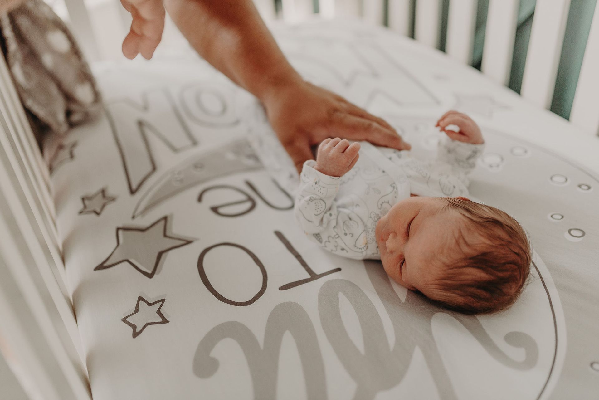 Parent gently placing a hand on a sleeping baby in a crib during nap time.