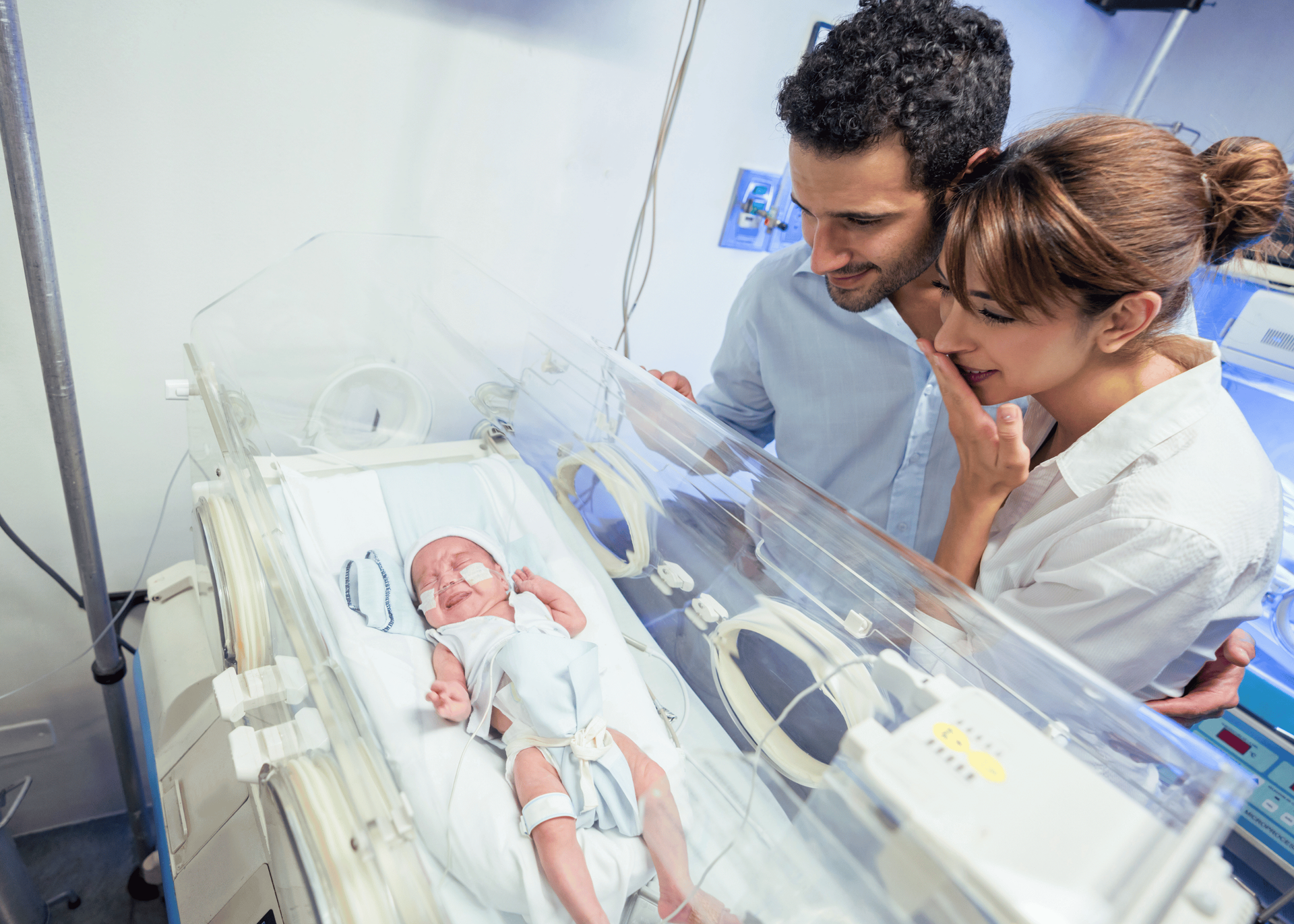 A couple observes their newborn in an incubator, conveying love and concern.