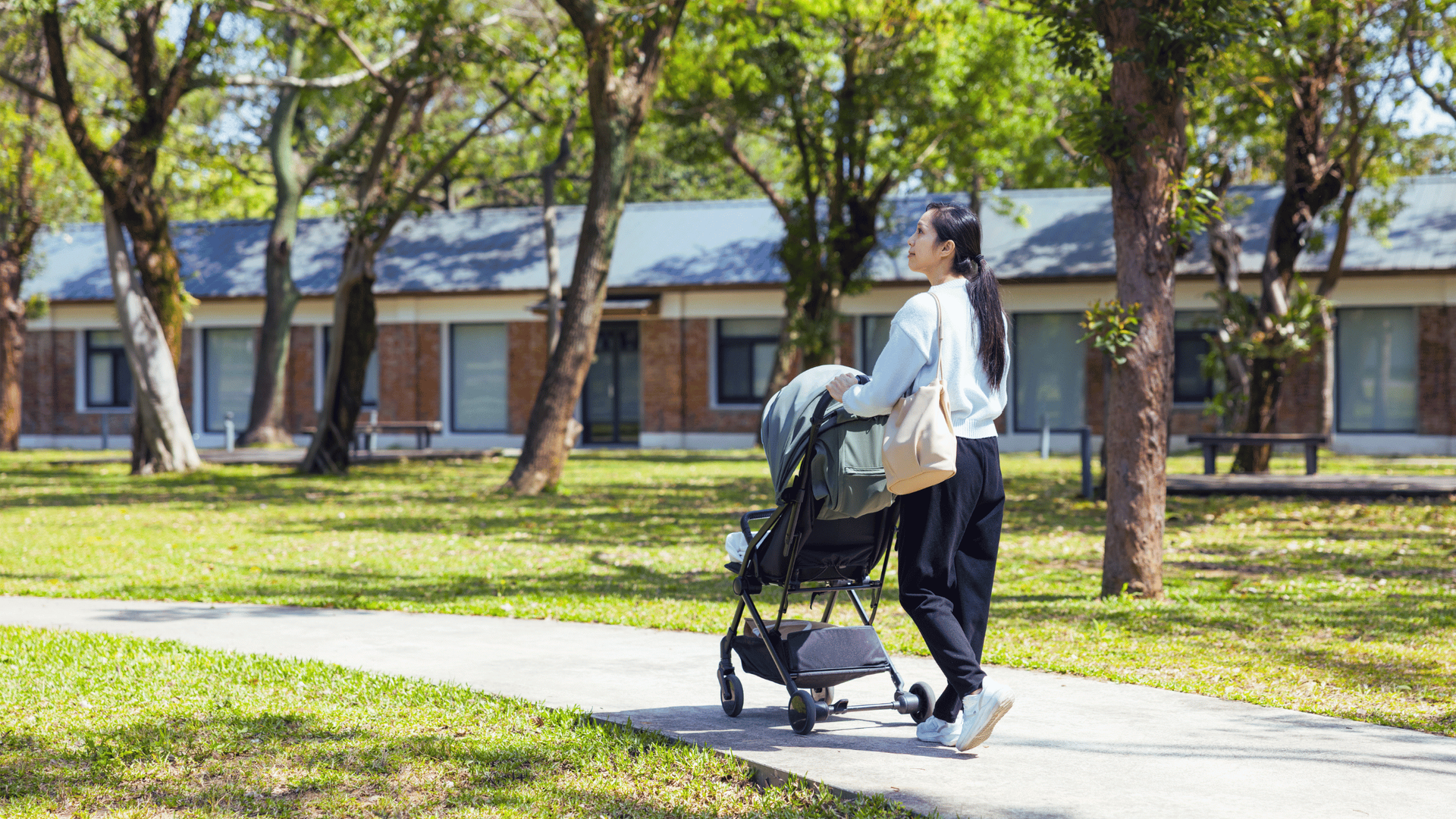A woman with a stroller walking on a sidewalk, enjoying a pleasant day in a neighborhood setting.