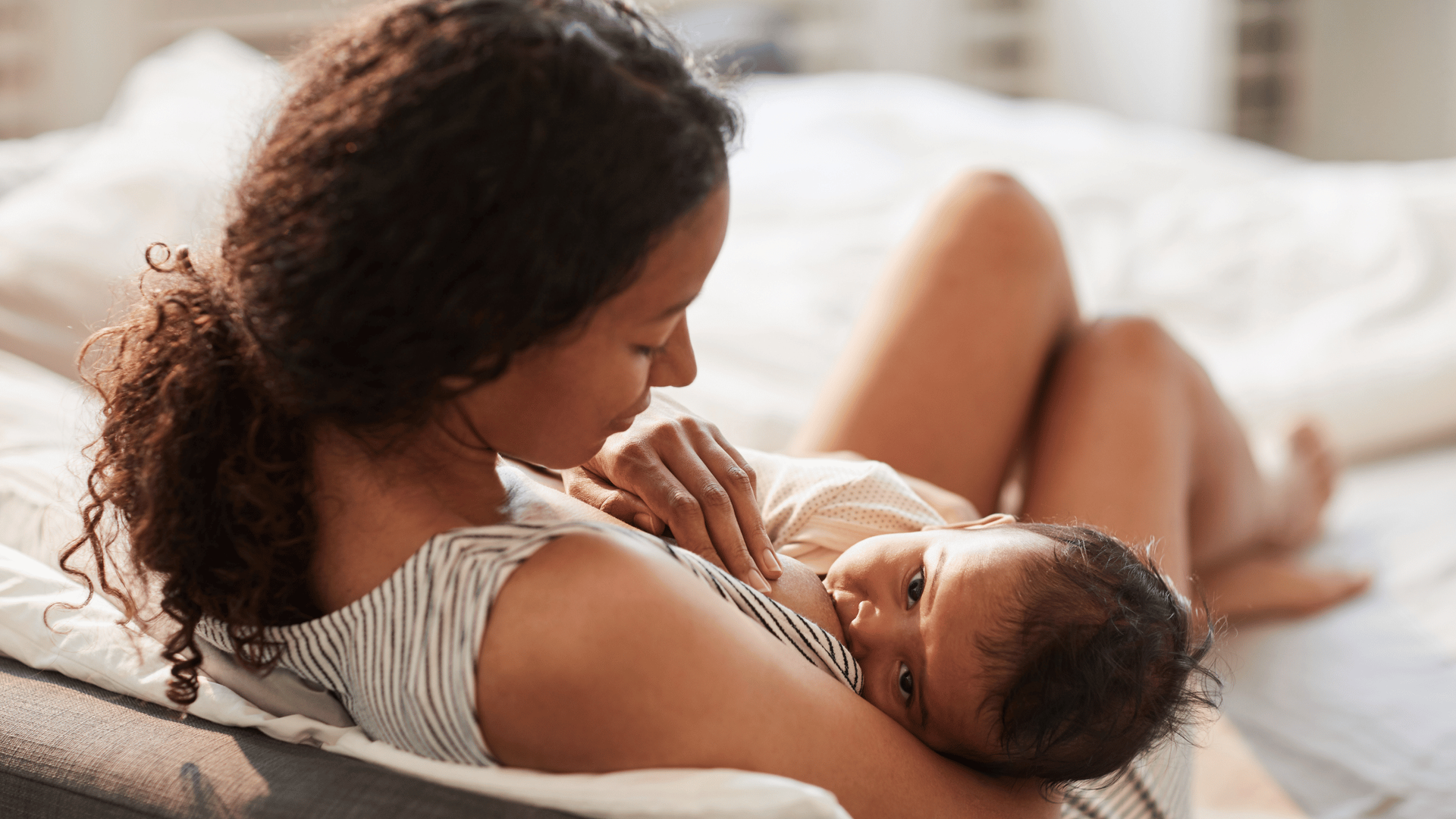 Mother cuddles her baby on a bed, gazing down affectionately as the infant rests on her chest.