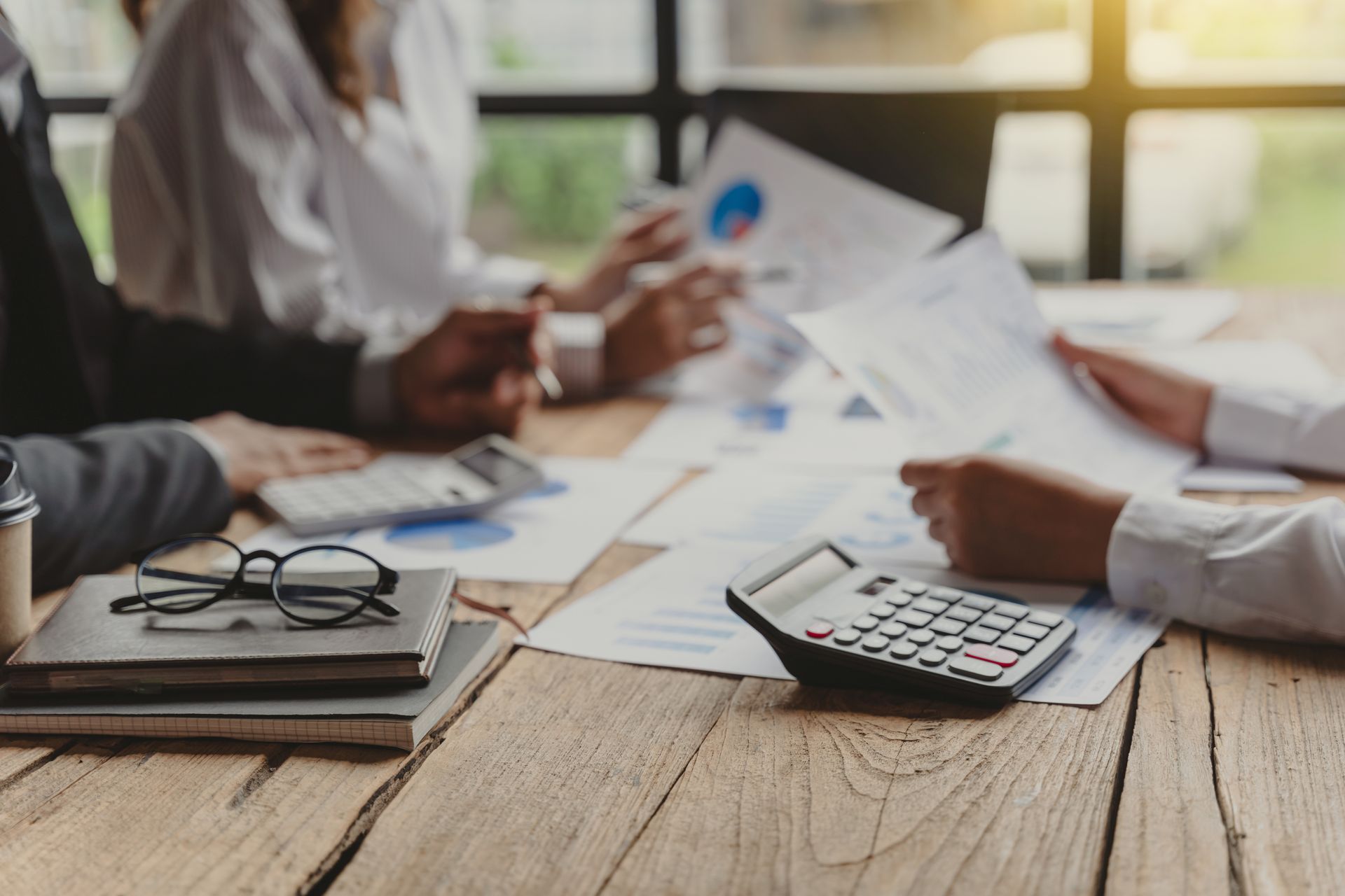 Three business people sit on a table with files and a calculator.