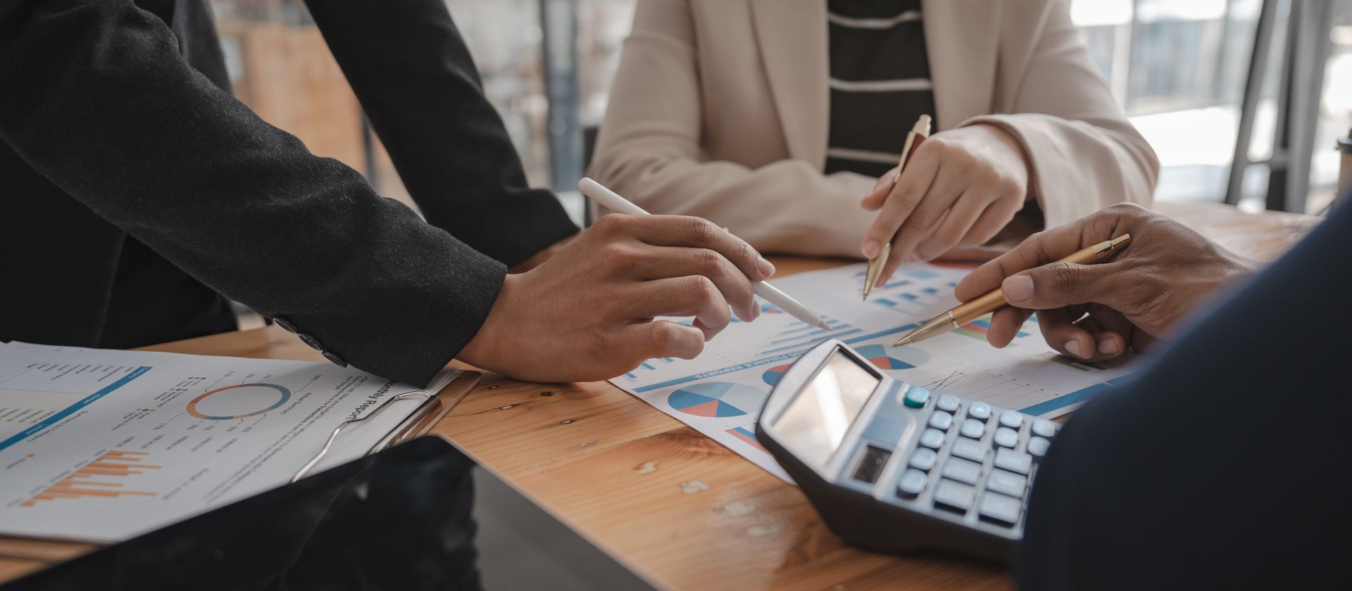 Three accountants reviewing financial charts and graphs with pens and a calculator at a wood desk