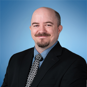 Studio portrait of a smiling man in a black suit and patterned tie on a blue background
