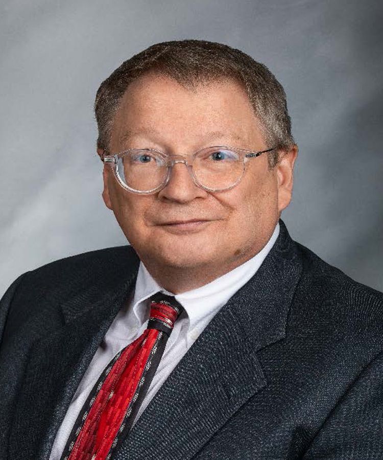 Man in suit and tie with glasses, looking at the viewer; studio portrait.