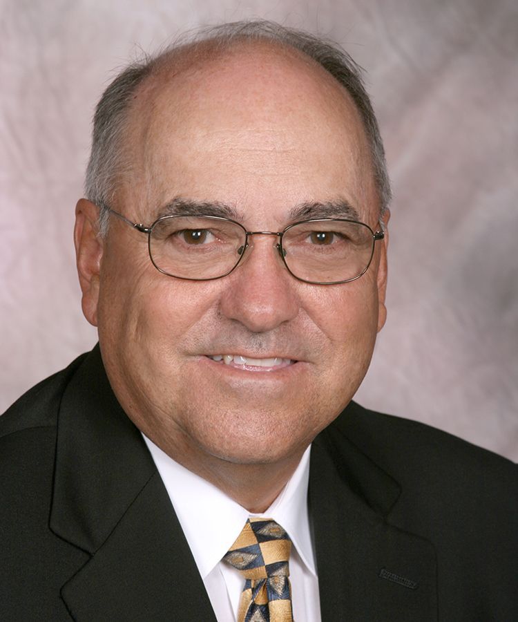 Man in glasses and suit, smiling, neutral background.