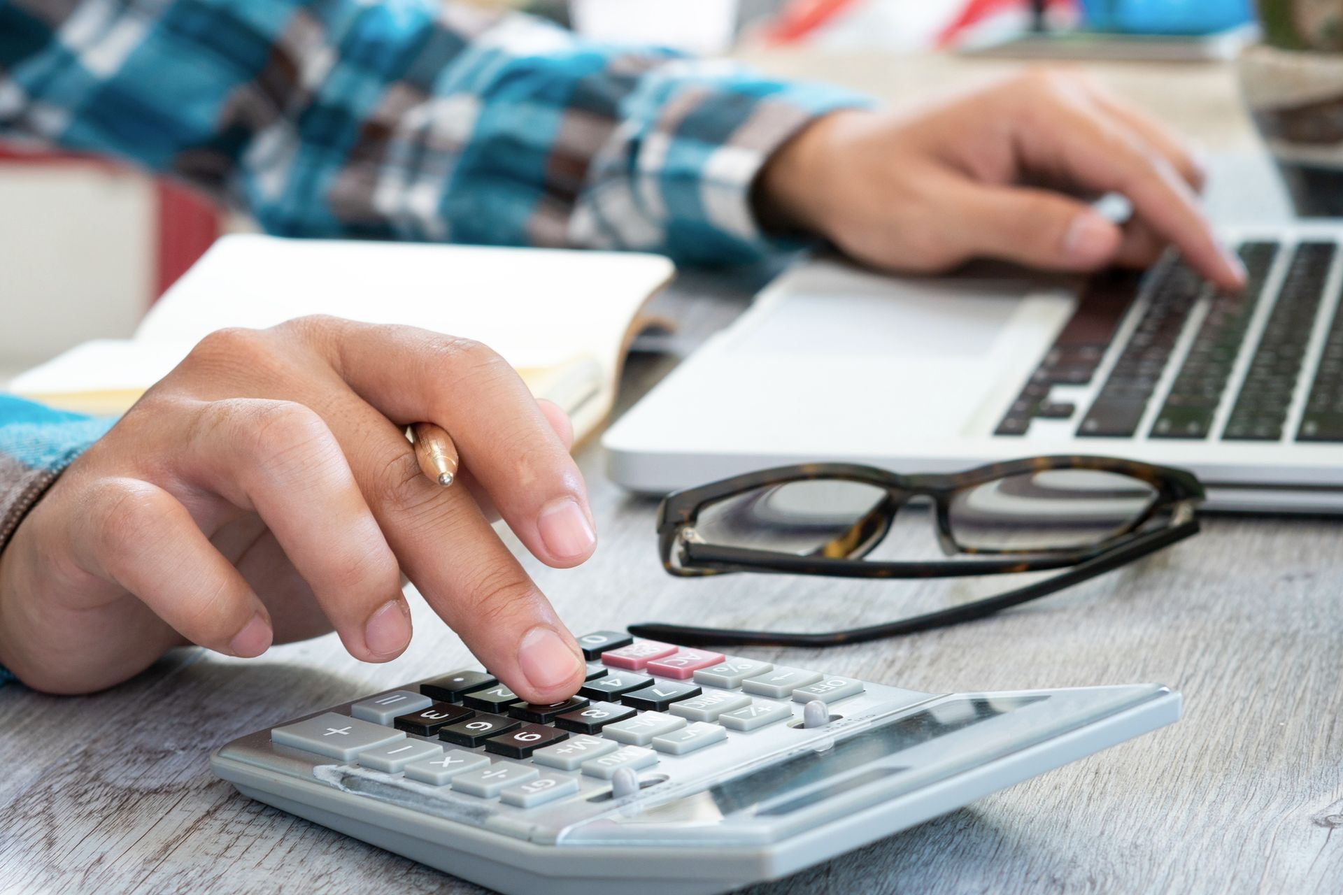 Person using calculator and laptop for financial planning or budgeting at home office desk.