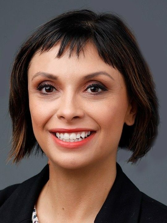 Woman with short, dark hair, smiling broadly, wearing a black blazer.