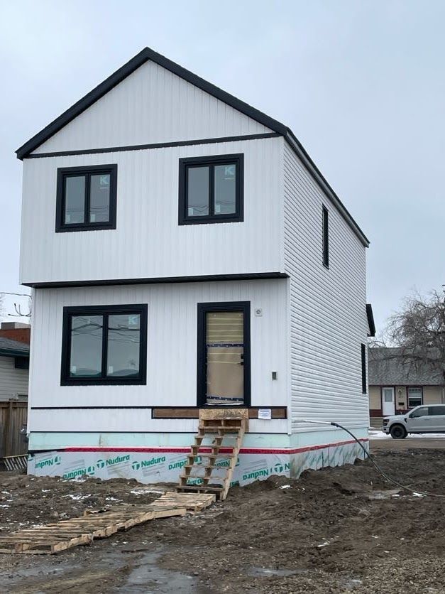Two-story house under construction, white siding, black trim, unfinished stairs, overcast sky.