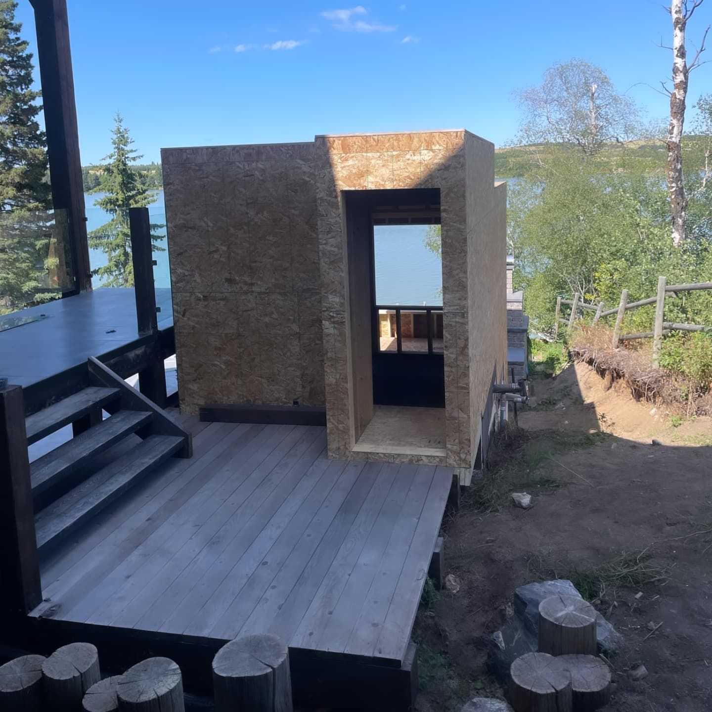 Wooden structure being built on a deck overlooking a lake, with stairs and natural surroundings.