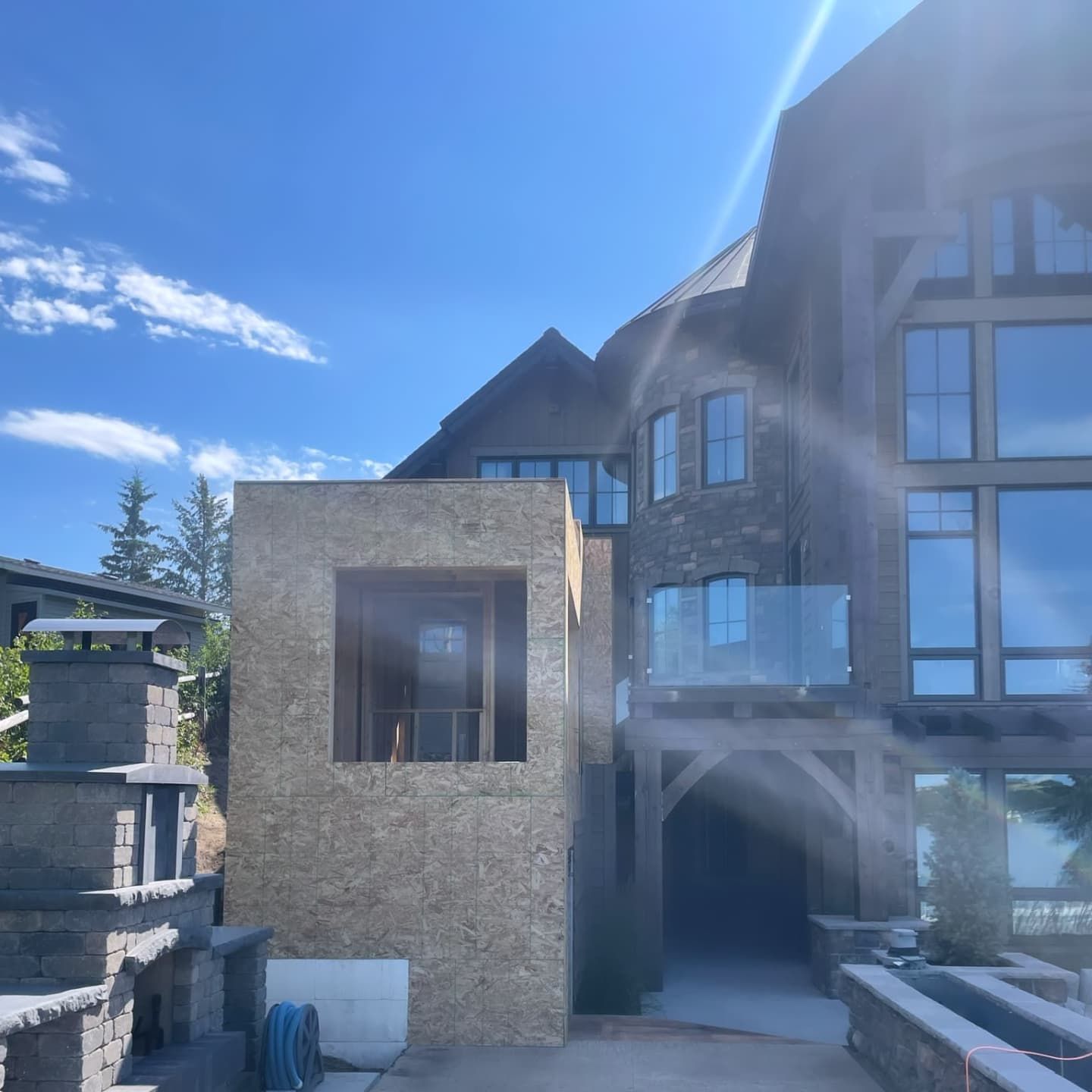 Exterior of a house under construction. A new framed wall is connected to a large multi-story building on a sunny day.