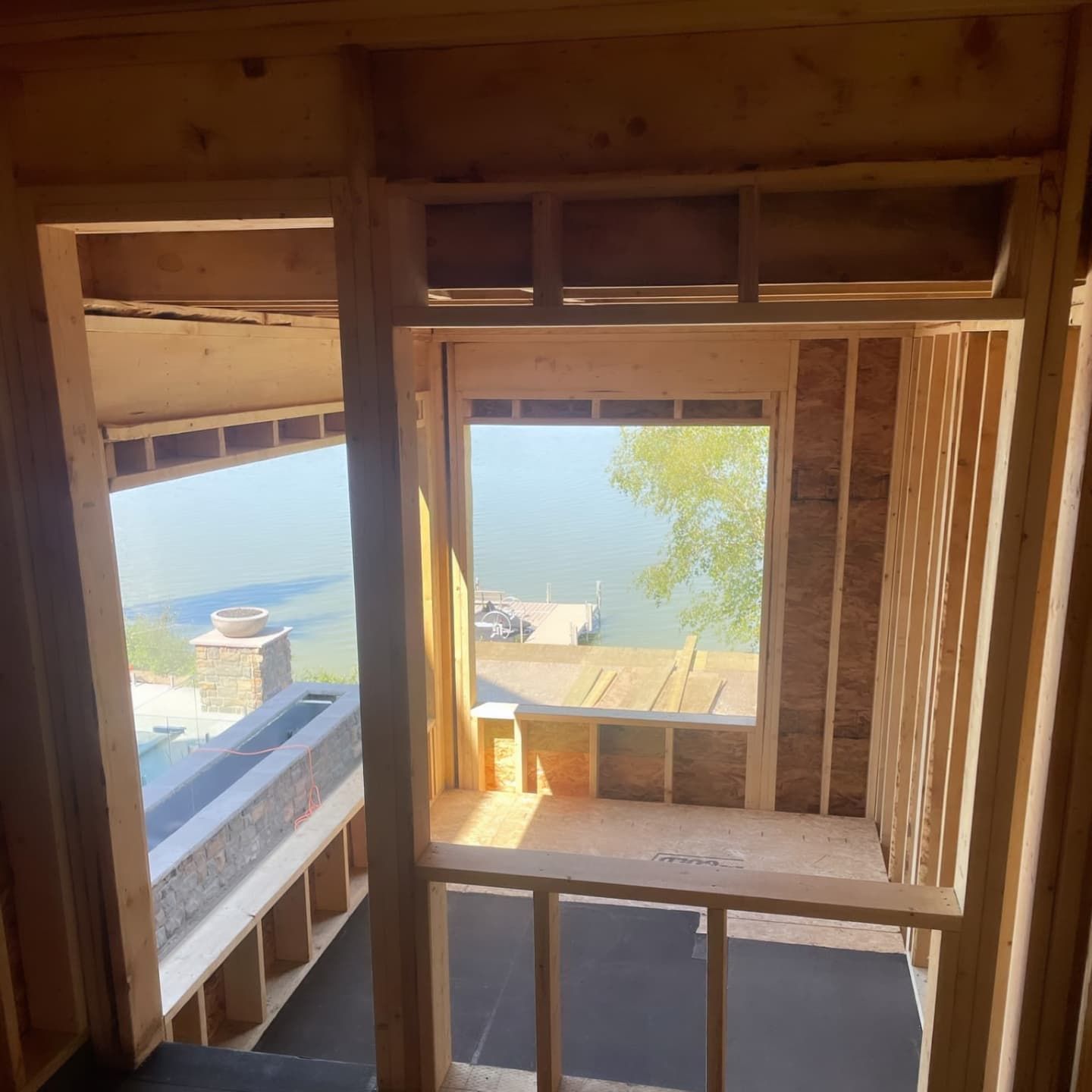 Interior construction showing wooden framing of windows and a room with a view of water and a dock.