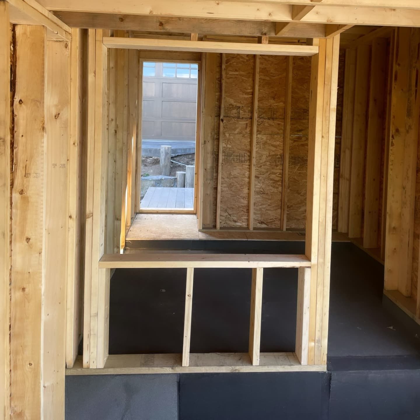 Interior view of wooden house framing with a window and doorway leading outside.