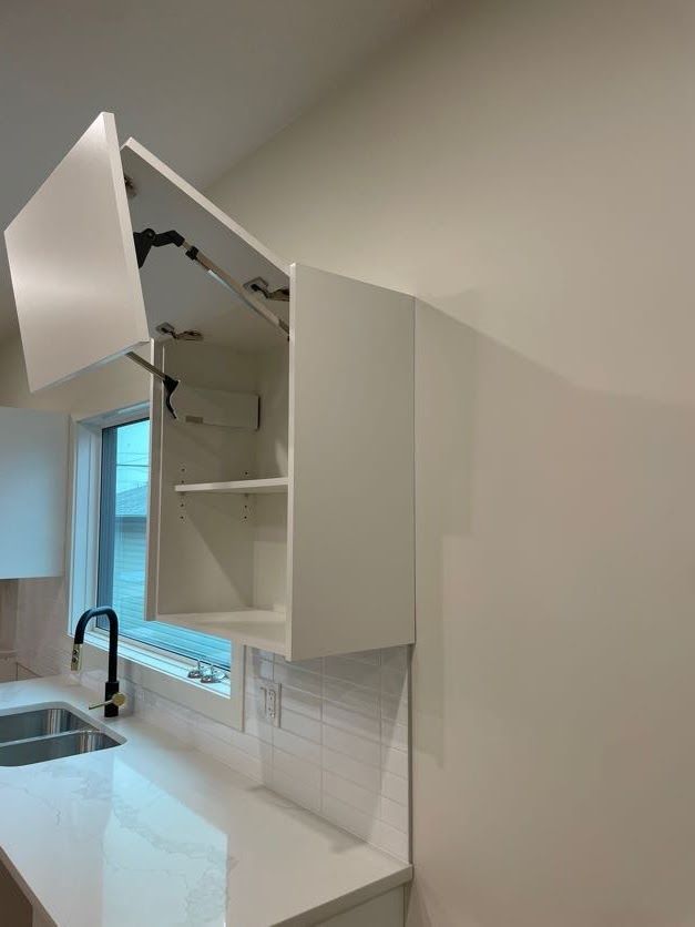 White kitchen cabinet with an open door, mounted above a countertop with a sink.