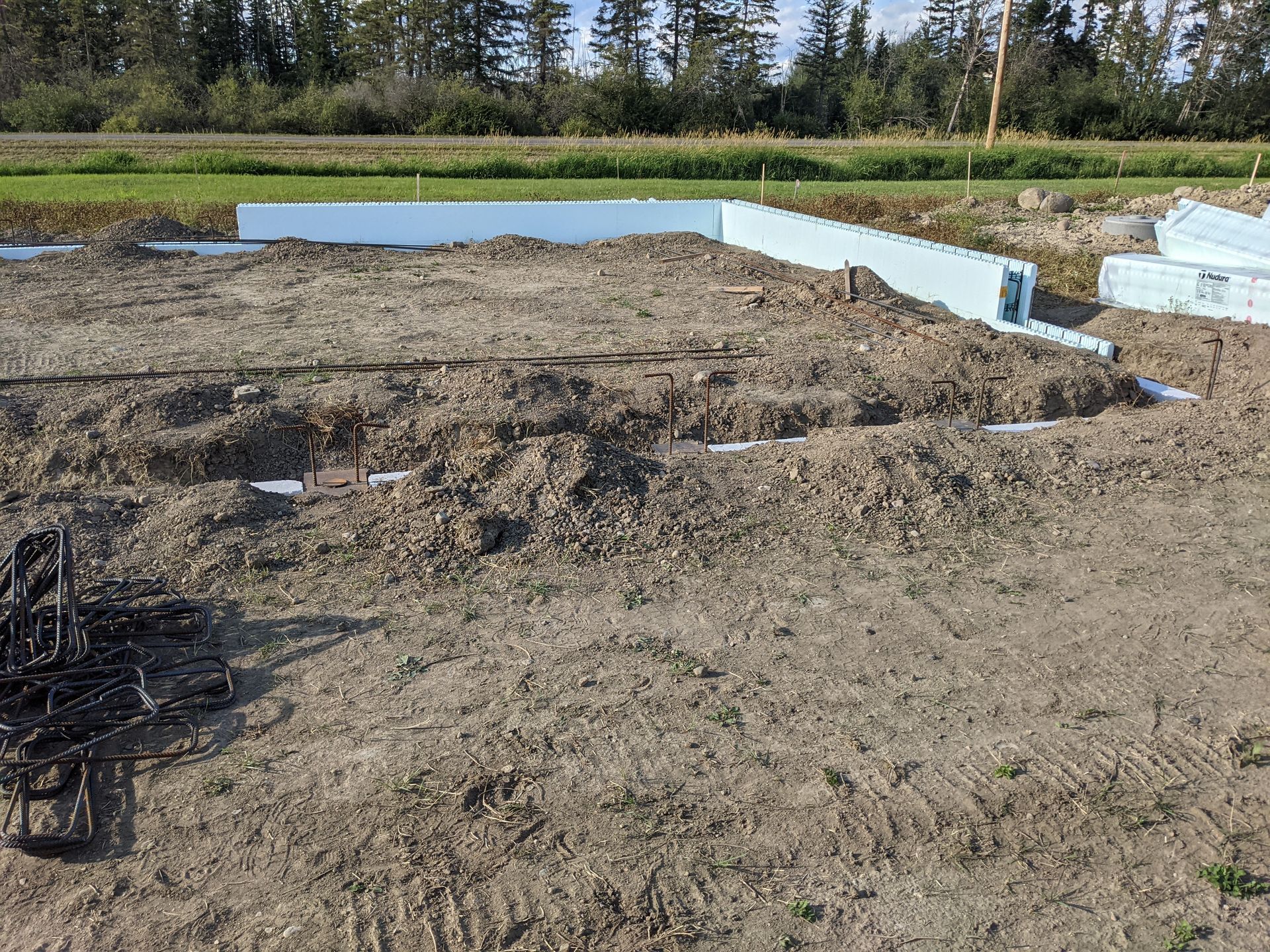 Construction site: Excavated dirt, blue foam foundation forms, and rebar on a field.