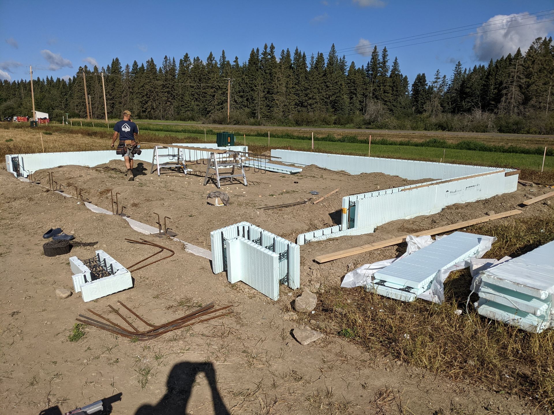 Construction site with ICF forms laid out, a man standing in the center. Earth and trees in the background.