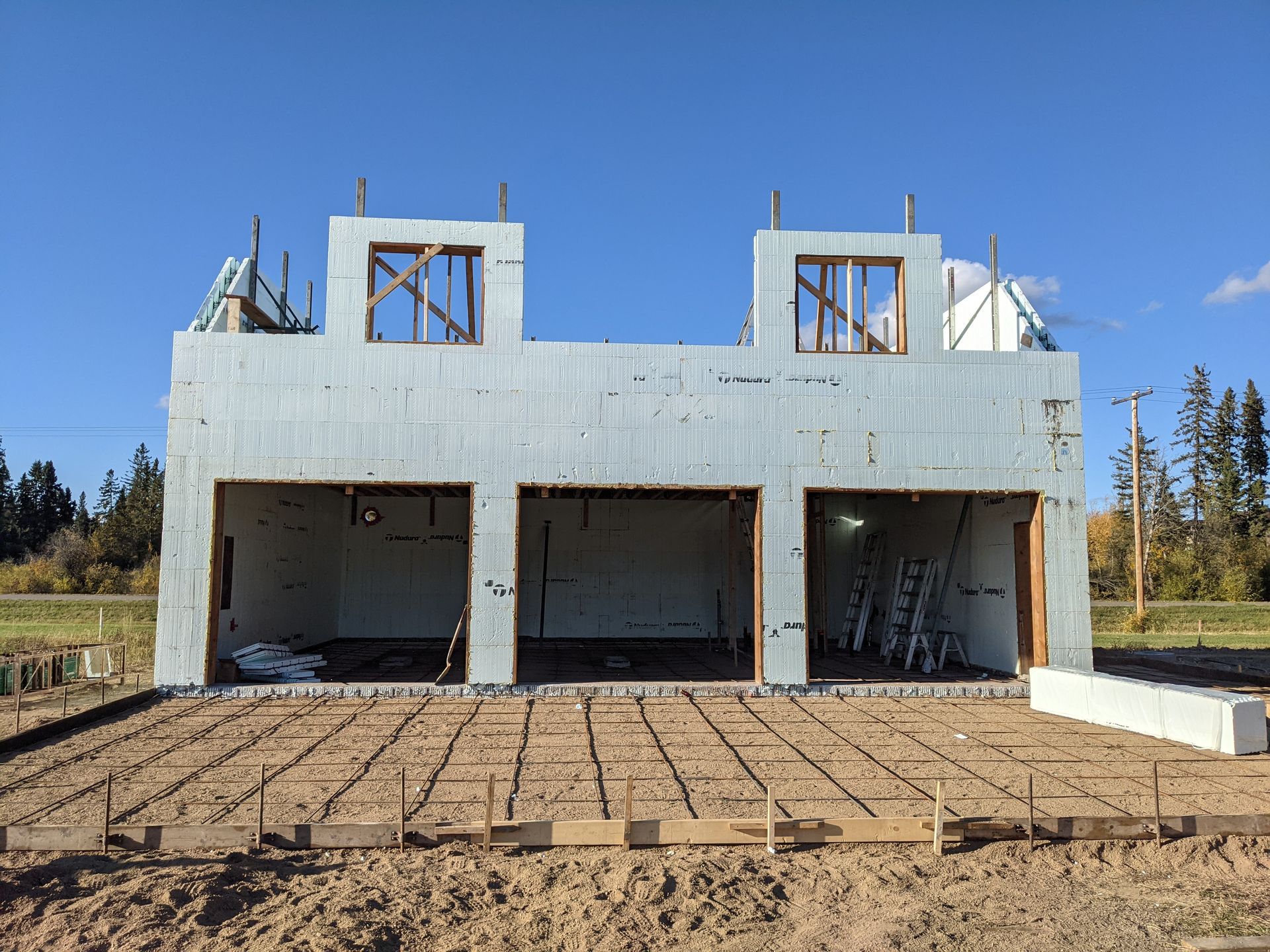 Construction site of a building with three garage bays; blue sky overhead.