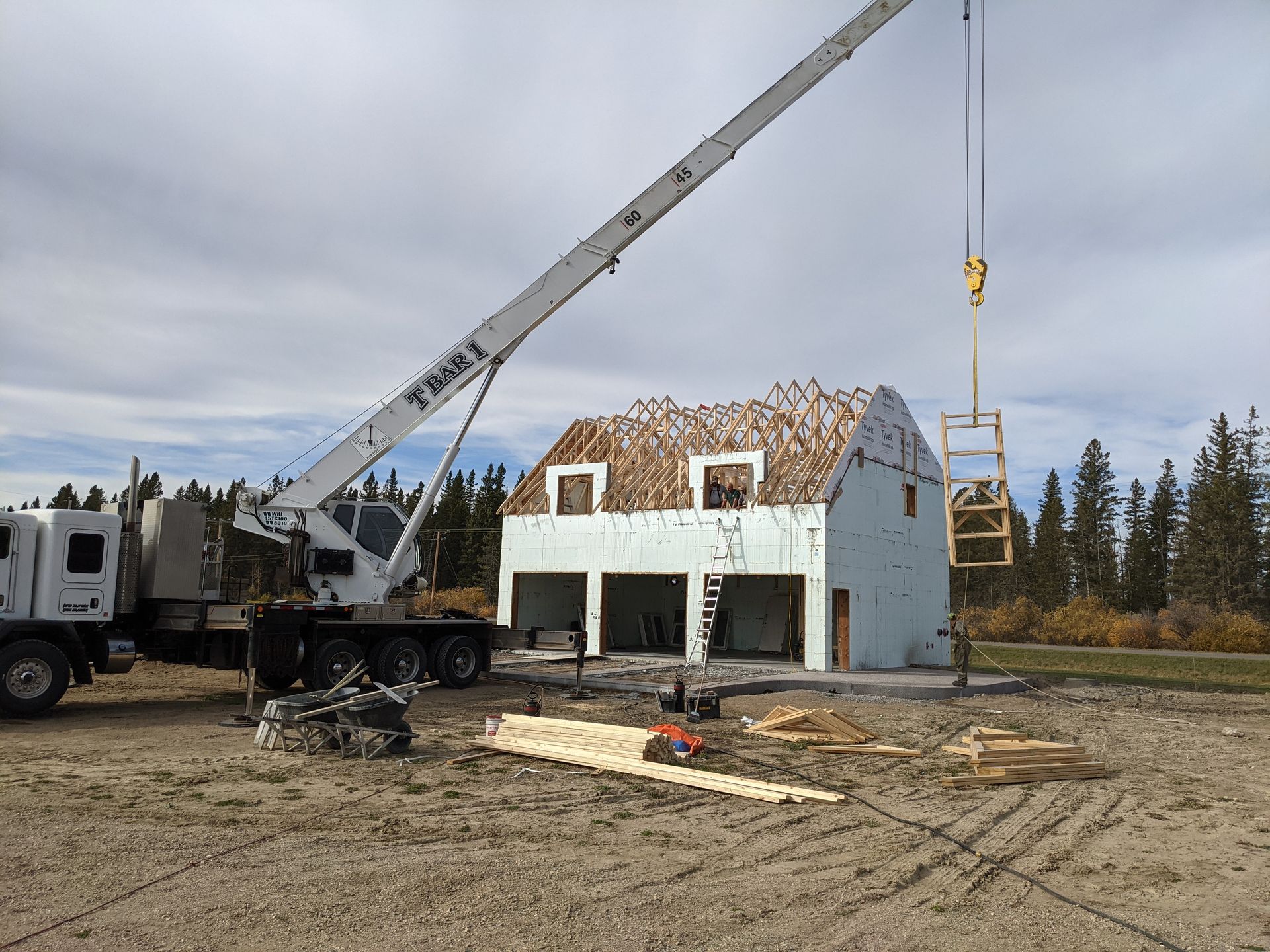 Construction site: crane lifting a wooden frame onto a two-story, white building with open garage bays.