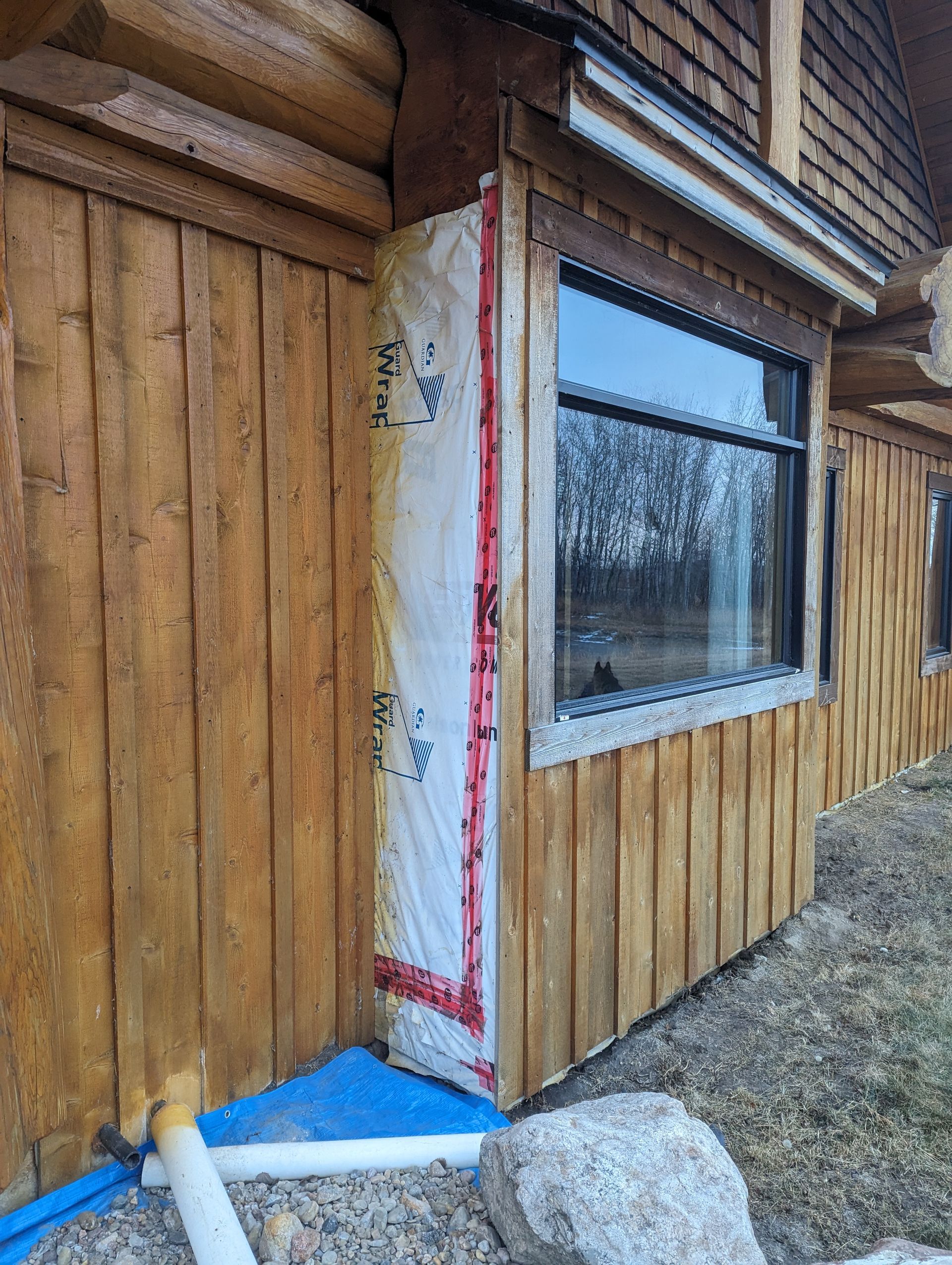 Exterior wall construction showing insulation around a window, next to a log cabin wall.