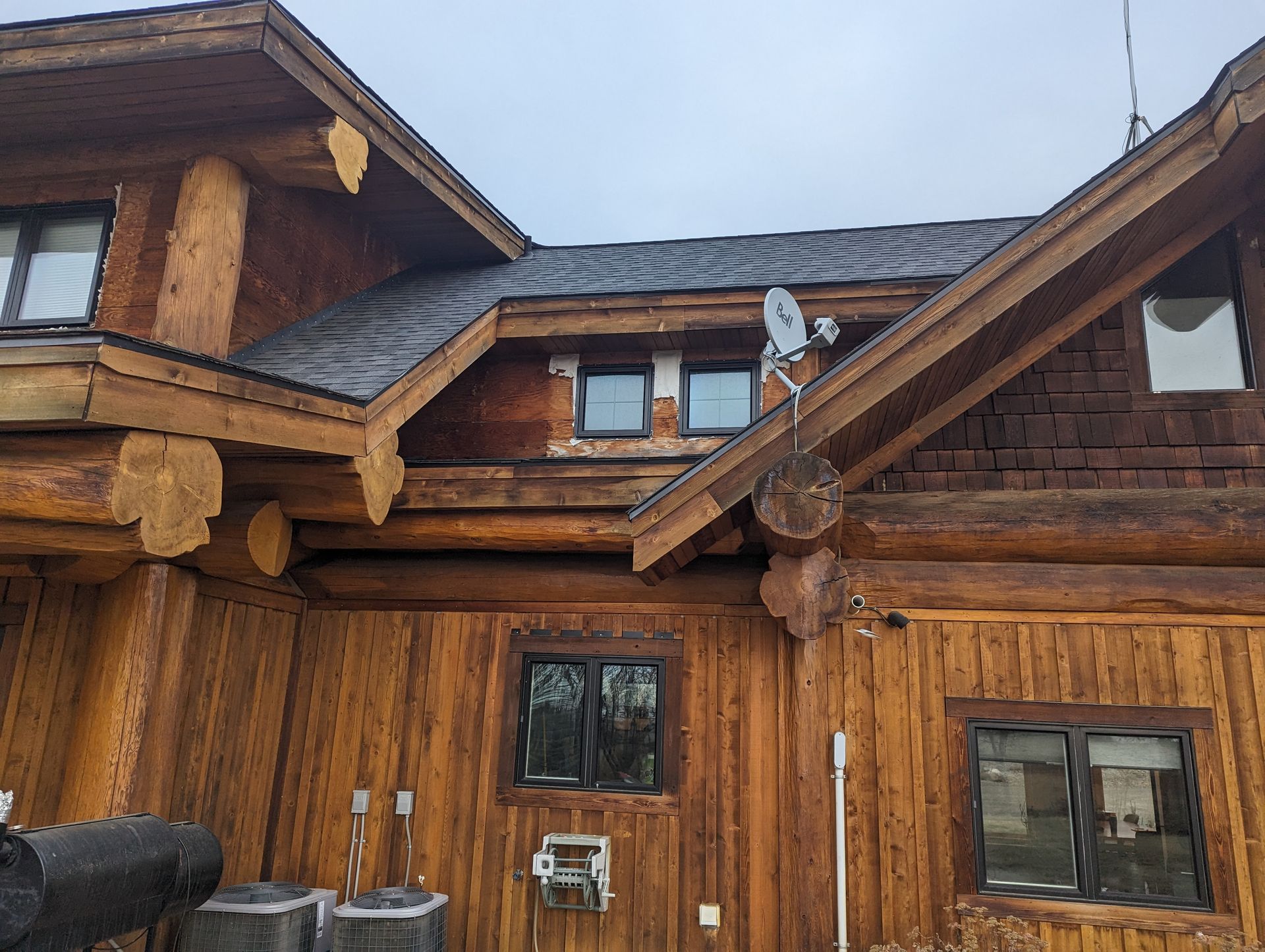 Log cabin exterior with wooden beams, dark roof, satellite dish, windows, and two outdoor air conditioning units.