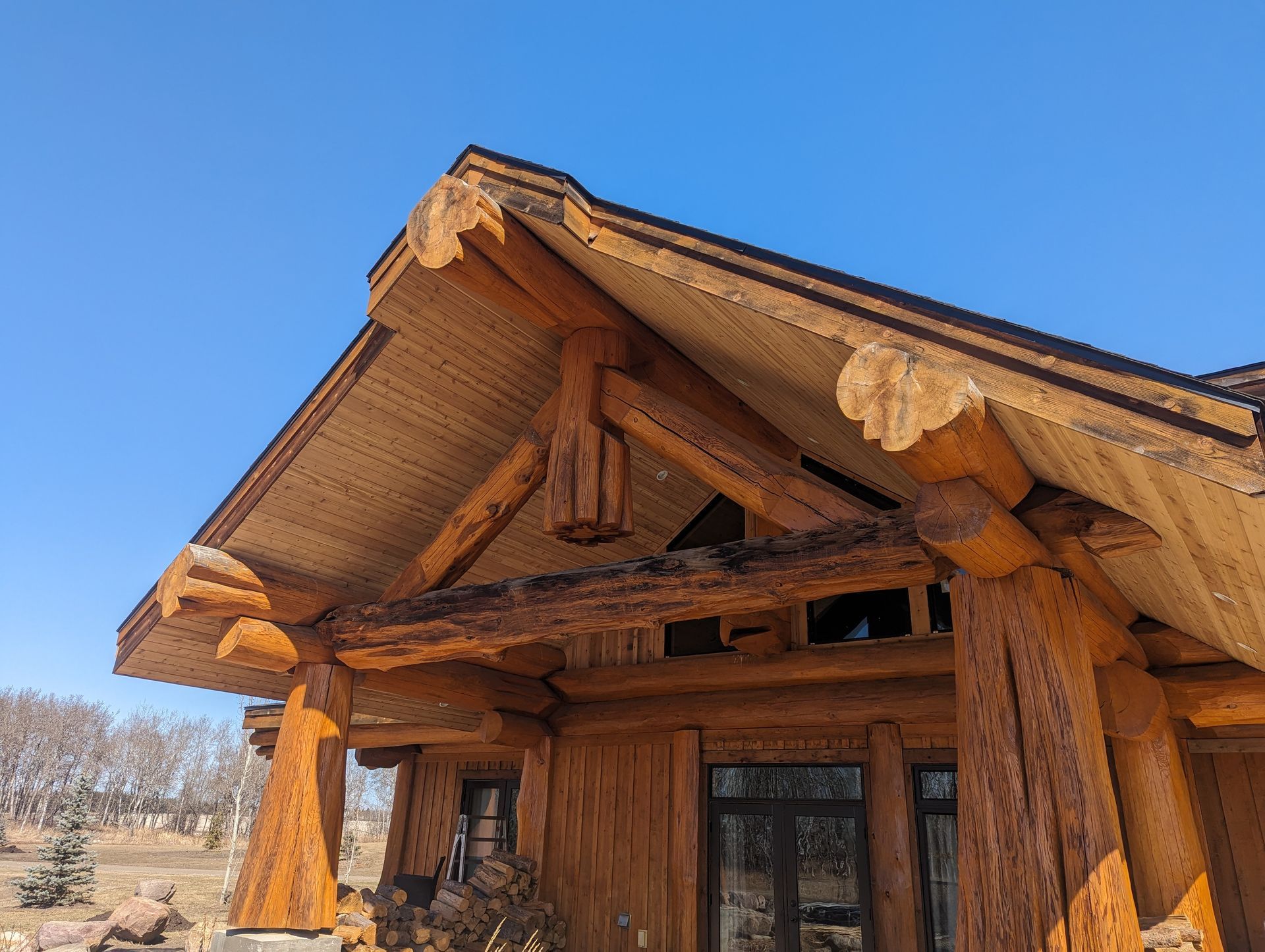 Wooden cabin porch with decorative carved beams and blue sky background.