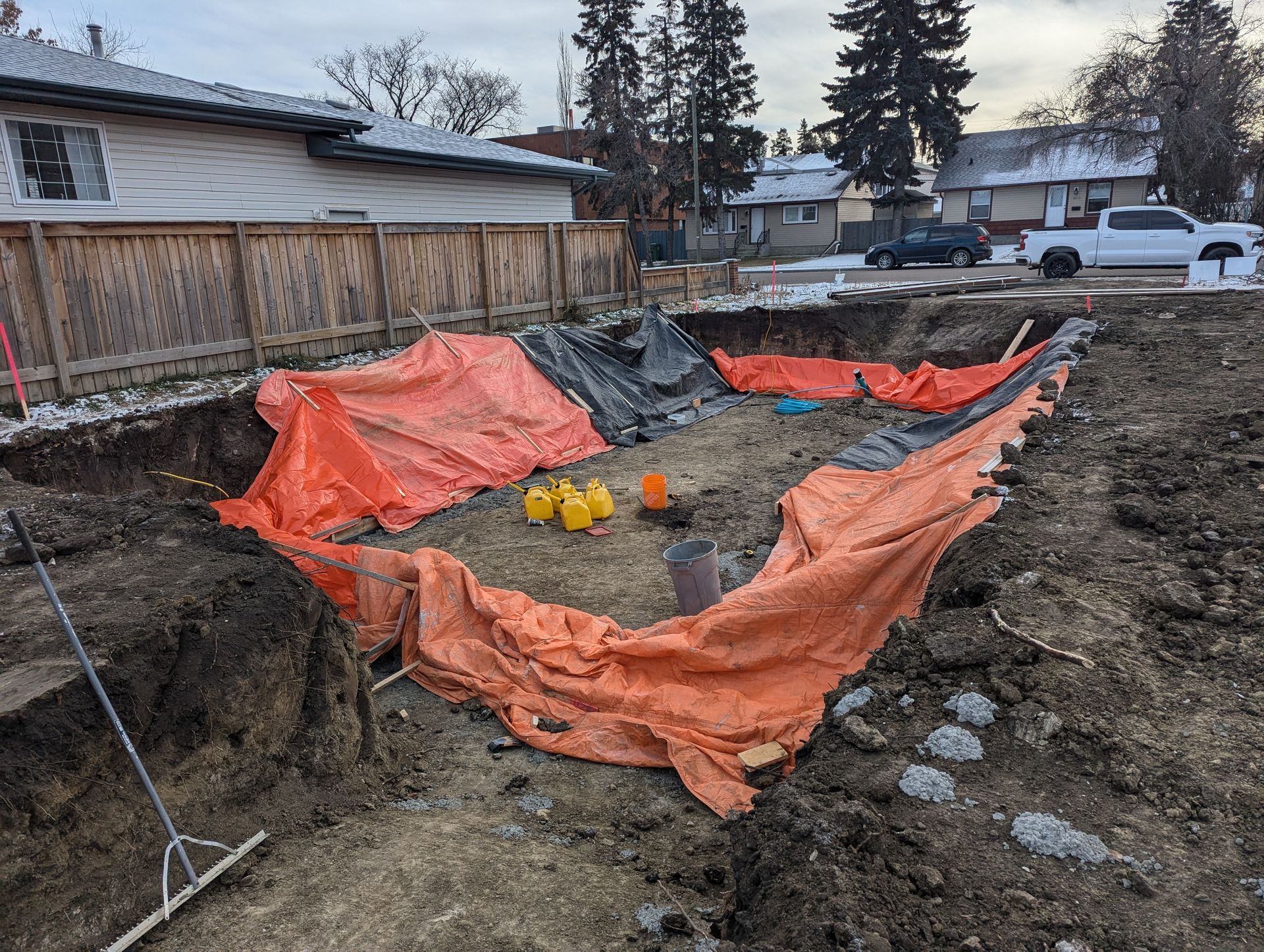 Construction site with an excavated area covered by orange tarps, surrounded by dirt and debris.