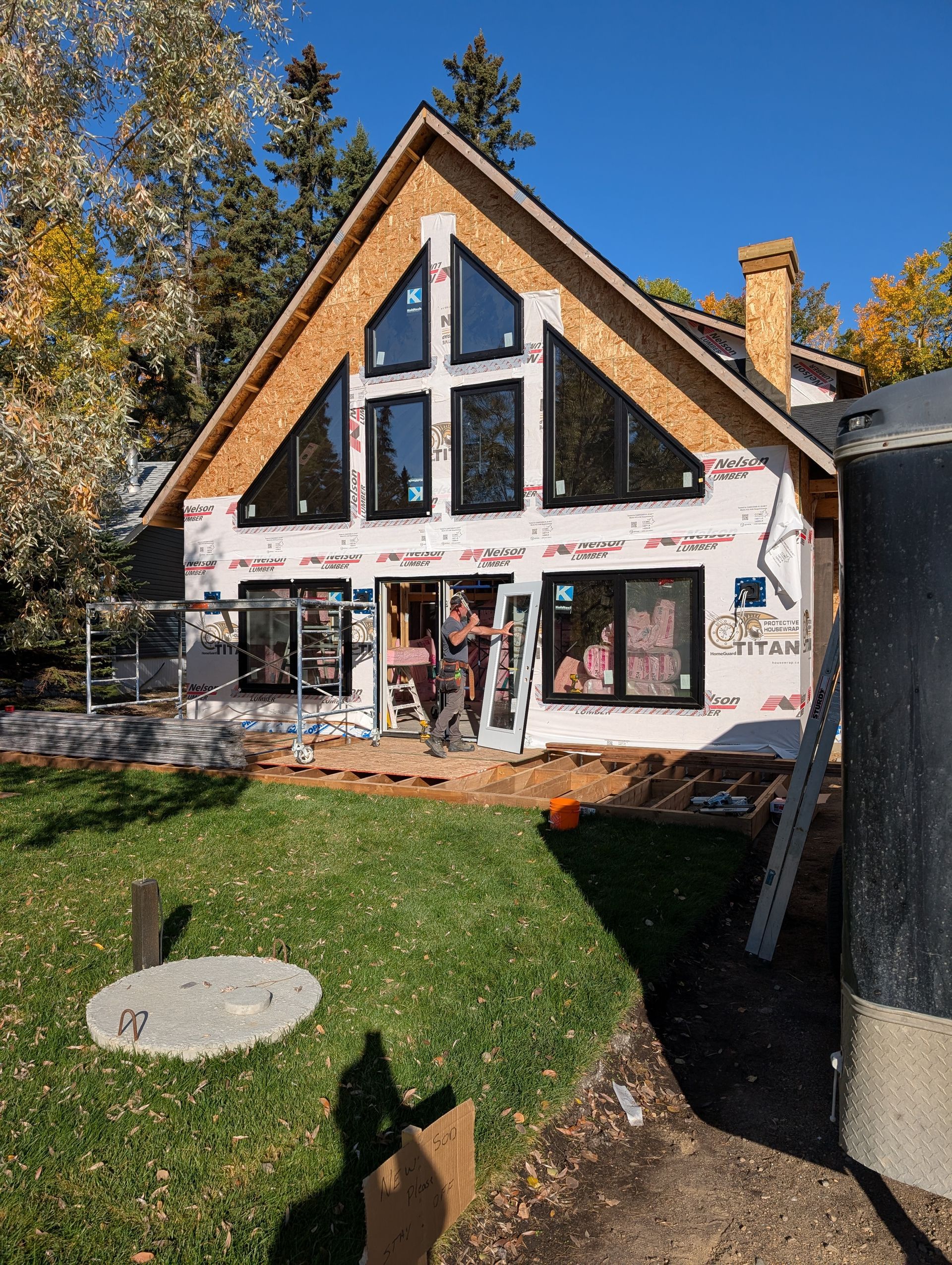 House under construction with large windows and A-frame roof; trees in the background.