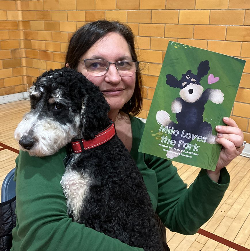 A woman is holding a dog and a book titled milo loves the park