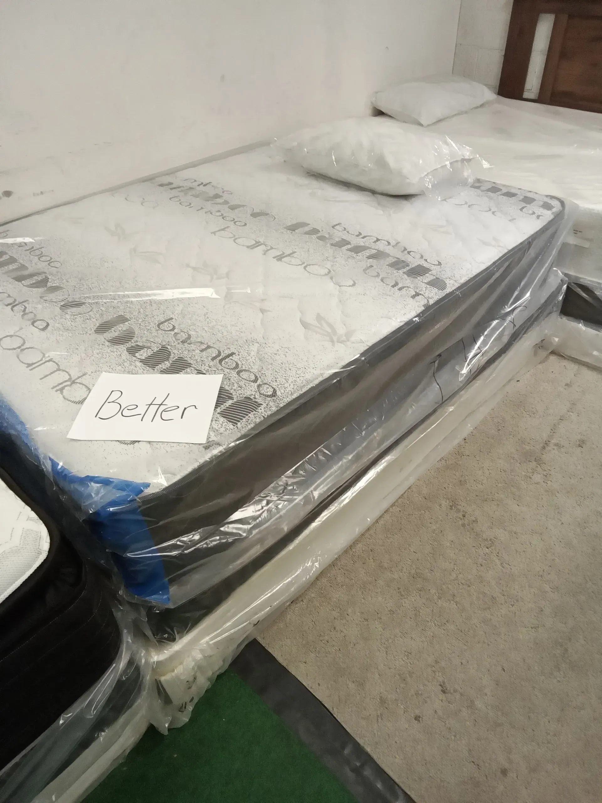 Mattress in plastic wrap with two pillows, displayed on a store floor with a small price tag.