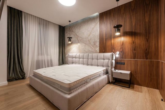 Modern bedroom with a large bed, wood-paneled wall, marble accent, and floor-to-ceiling curtains