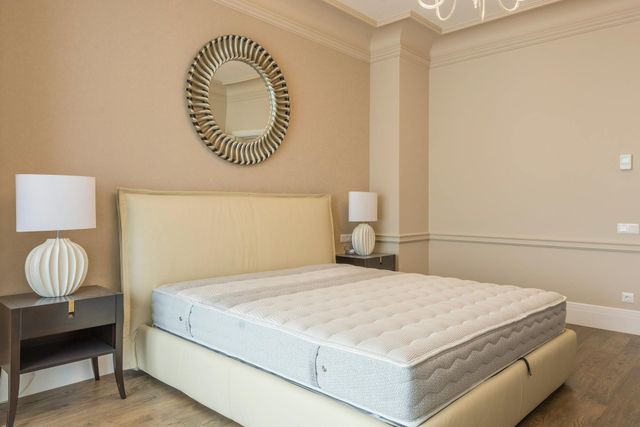 Neat beige bedroom with a bed, two lamps, and a round wall mirror