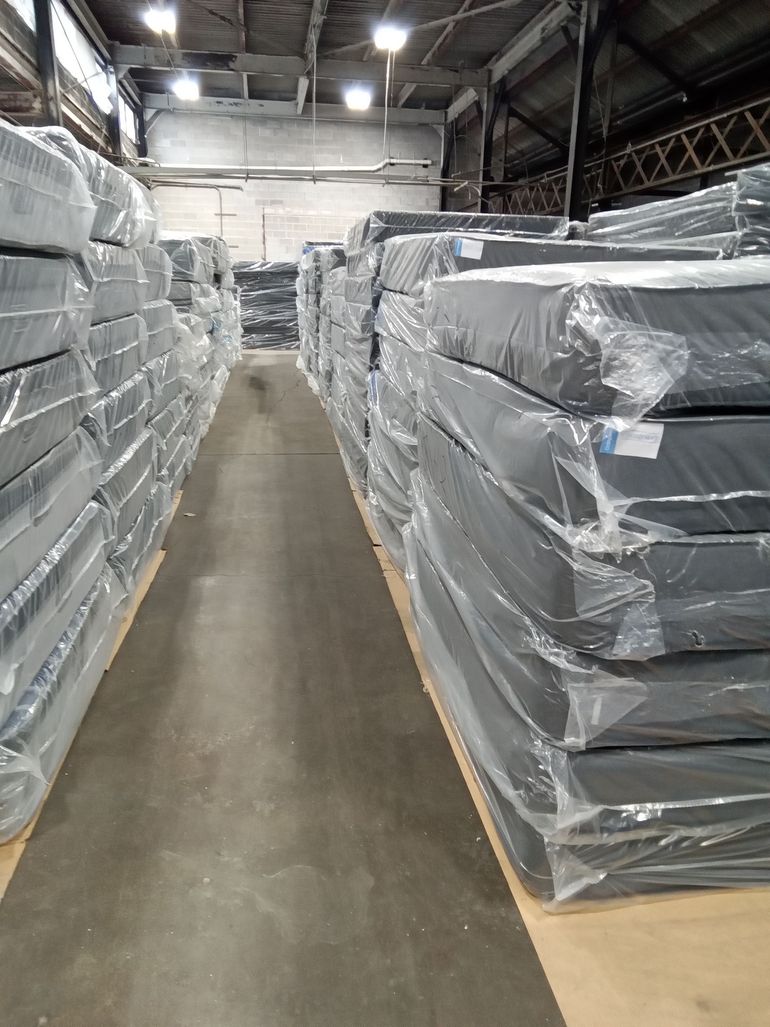 Warehouse aisle with stacks of wrapped pallets on both sides under overhead lights