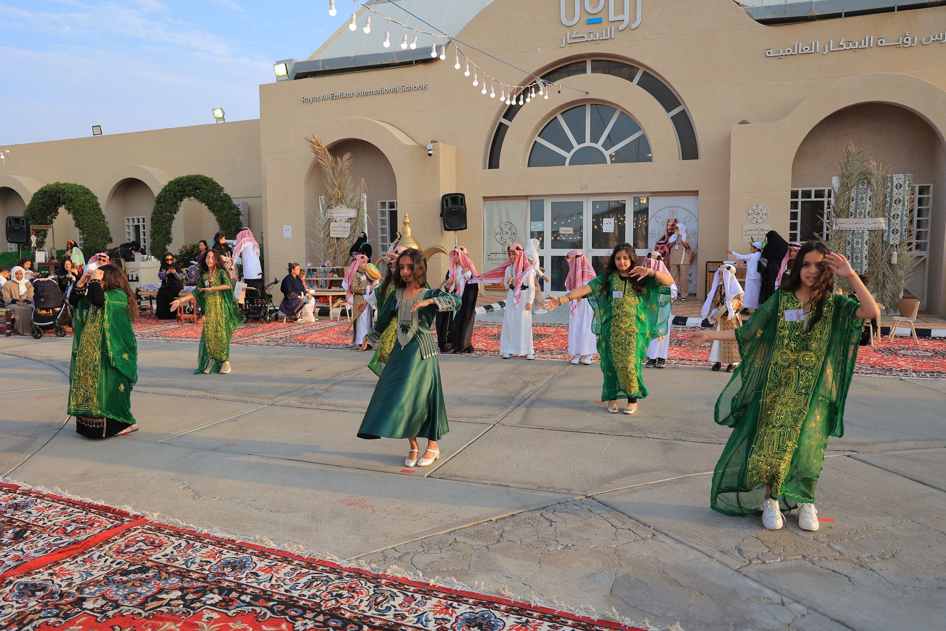 A group of women in green dresses are dancing in front of a building.