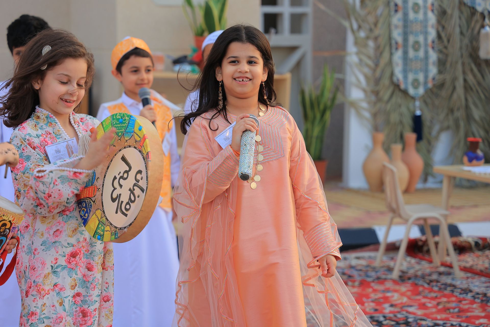 A girl is singing into a microphone while another girl plays a drum.