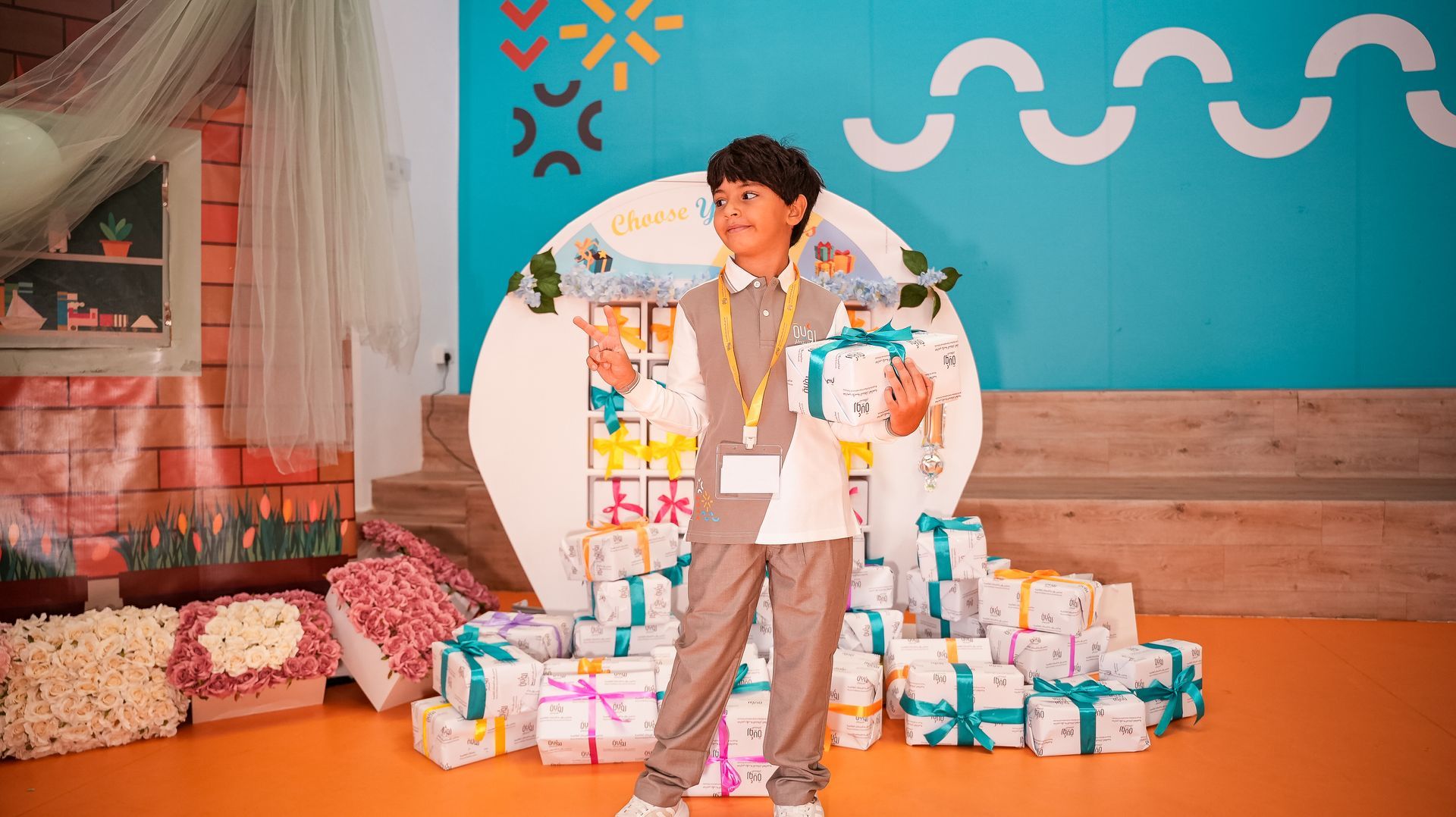 Boy standing among wrapped gifts in a colorful party setting with blue wall and orange floor
