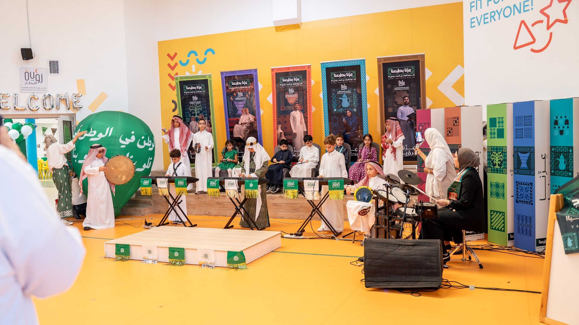 Students performing on a colorful school stage with drums, microphones, and decorative panels