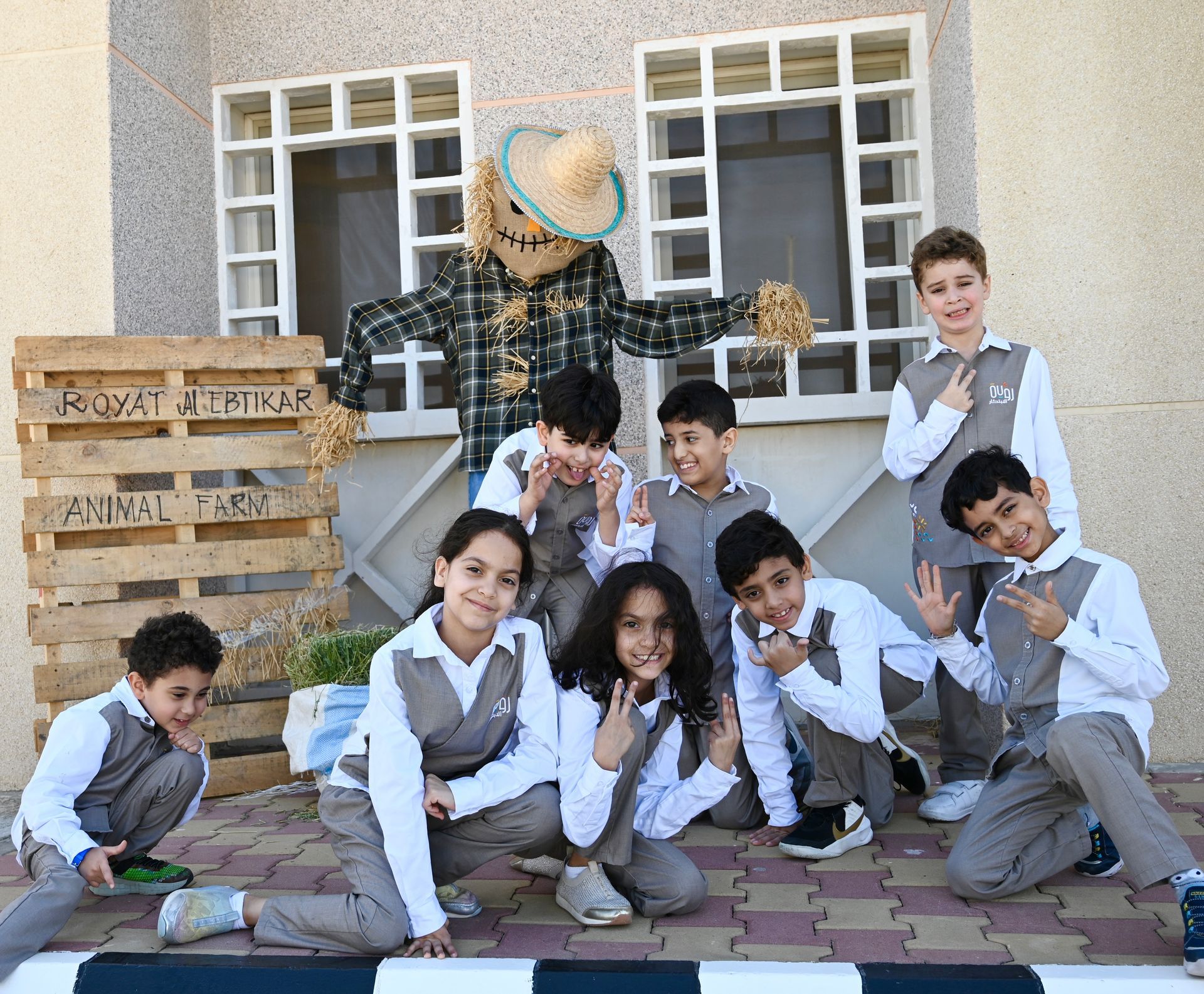 Students posing in matching gray uniforms in front of a decorated school display and windows