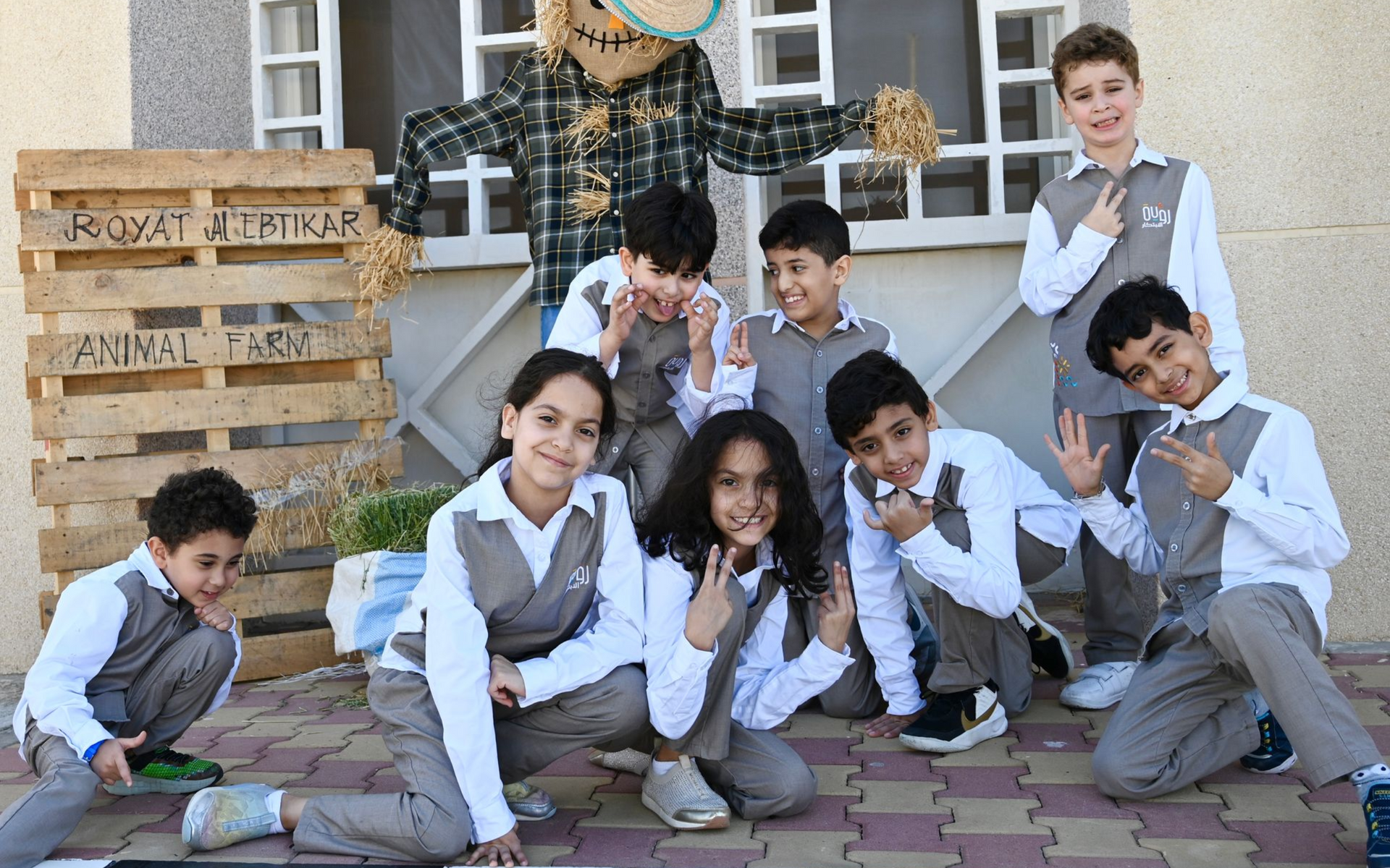 Children in white school uniforms posing with a decorated wooden pallet display outdoors