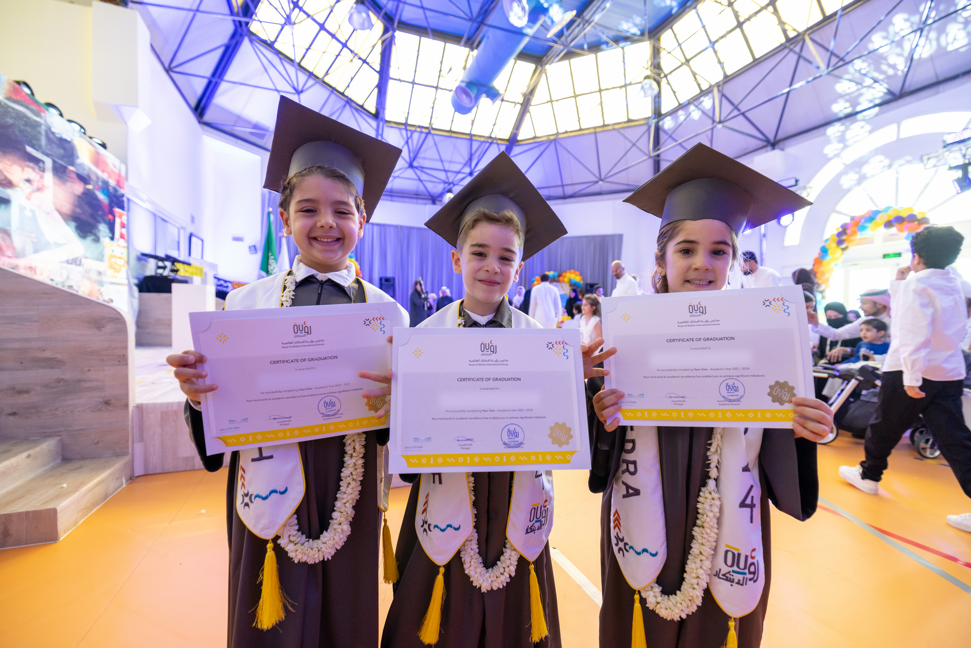 Three children in graduation caps and gowns are holding up their diplomas.