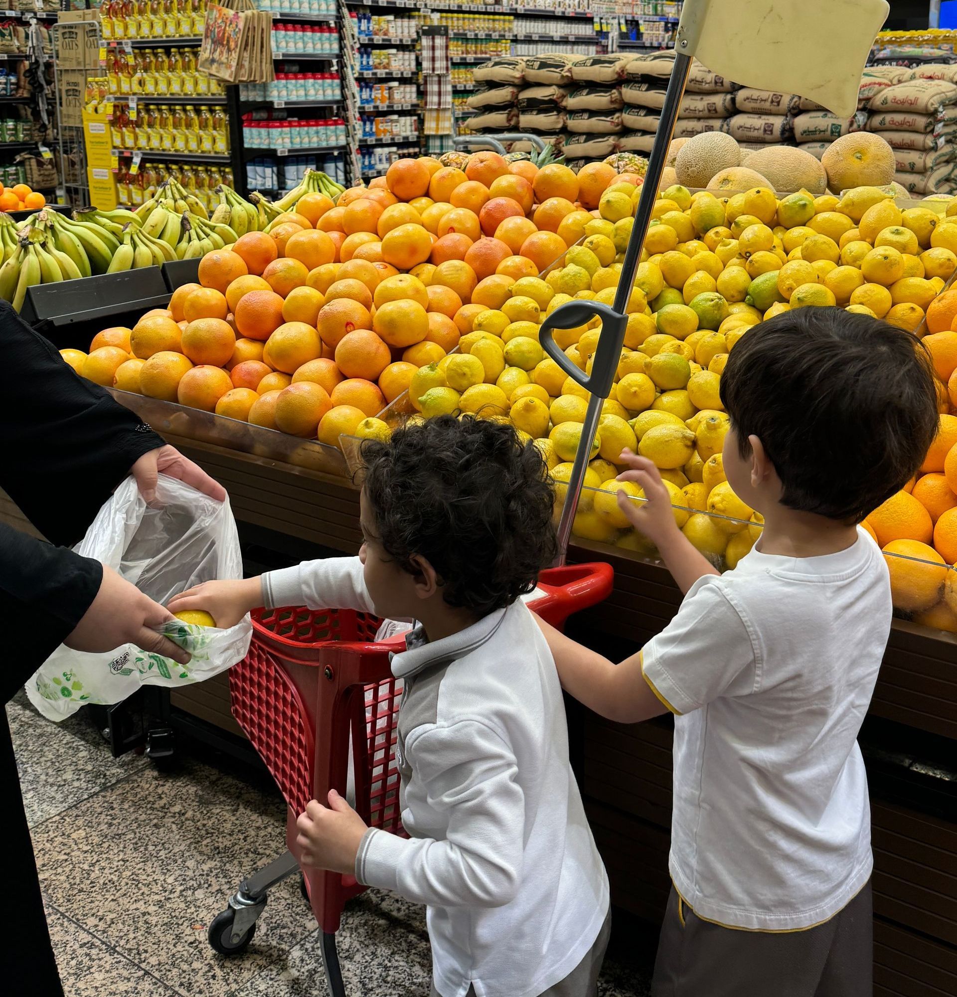 Two young boys are standing in front of a fruit stand in a grocery store.