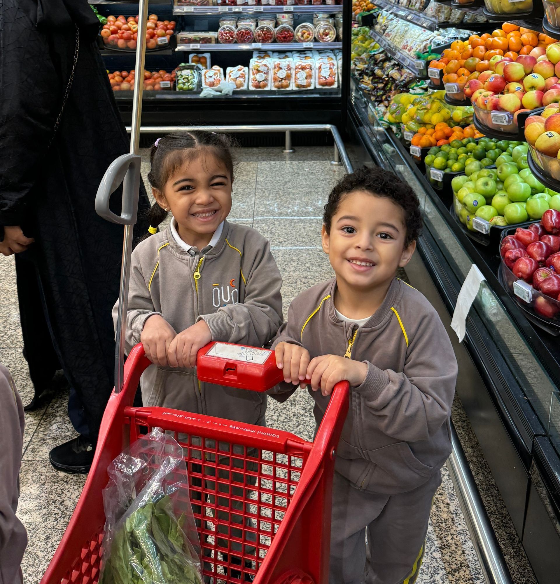 Two children are pushing a shopping cart in a grocery store.