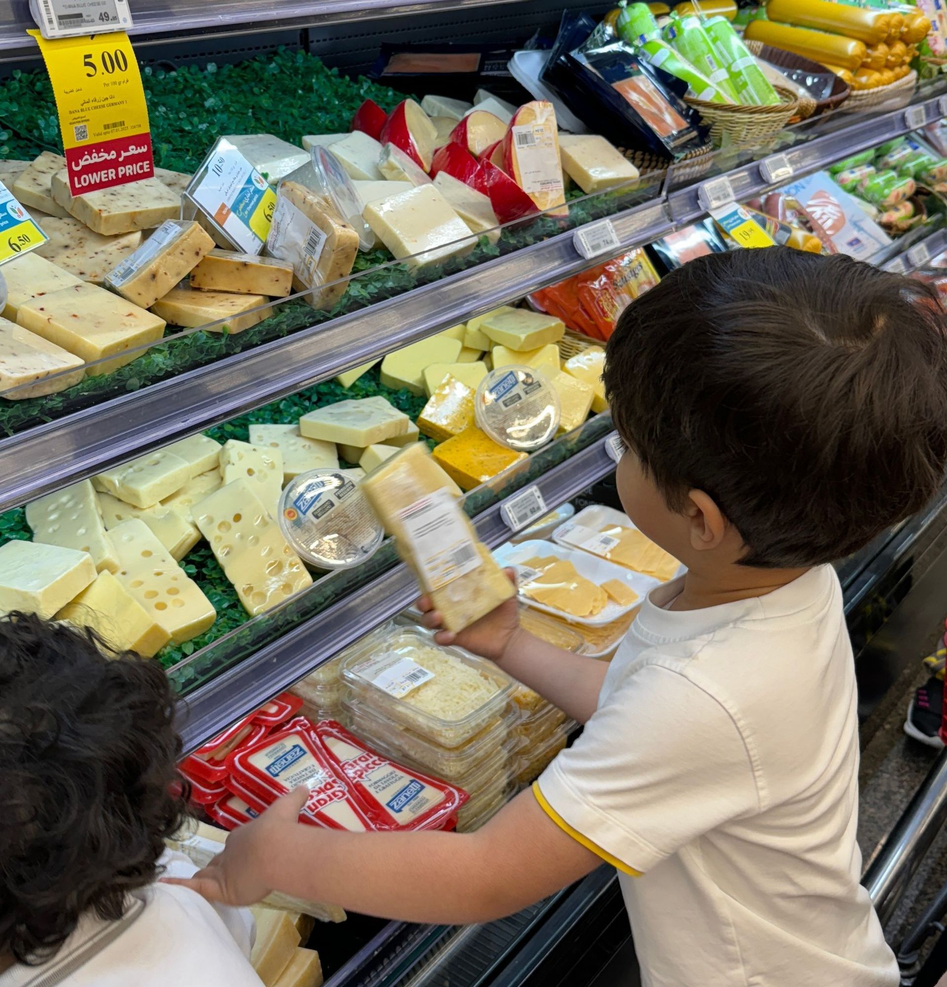 Two young children are looking at cheese in a grocery store.