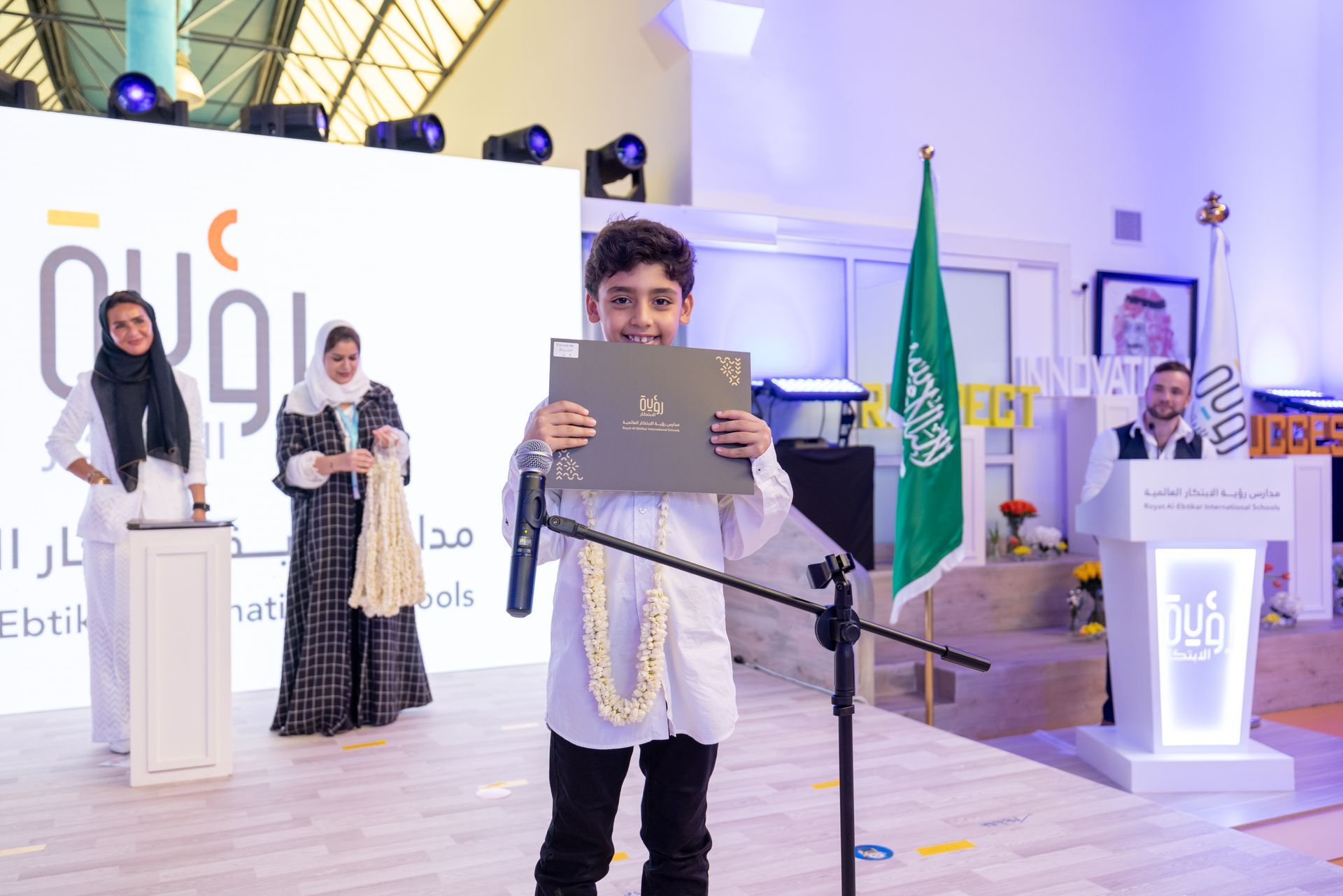 A young boy is standing in front of a microphone holding a certificate.