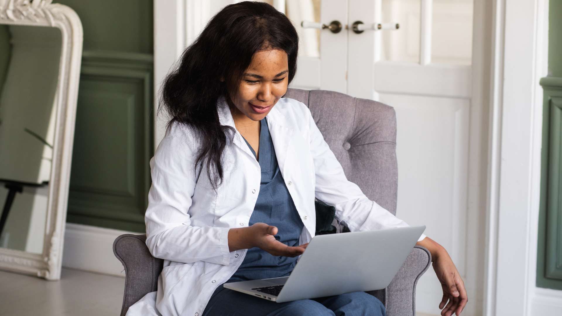 A female doctor is sitting in a chair using a laptop computer.