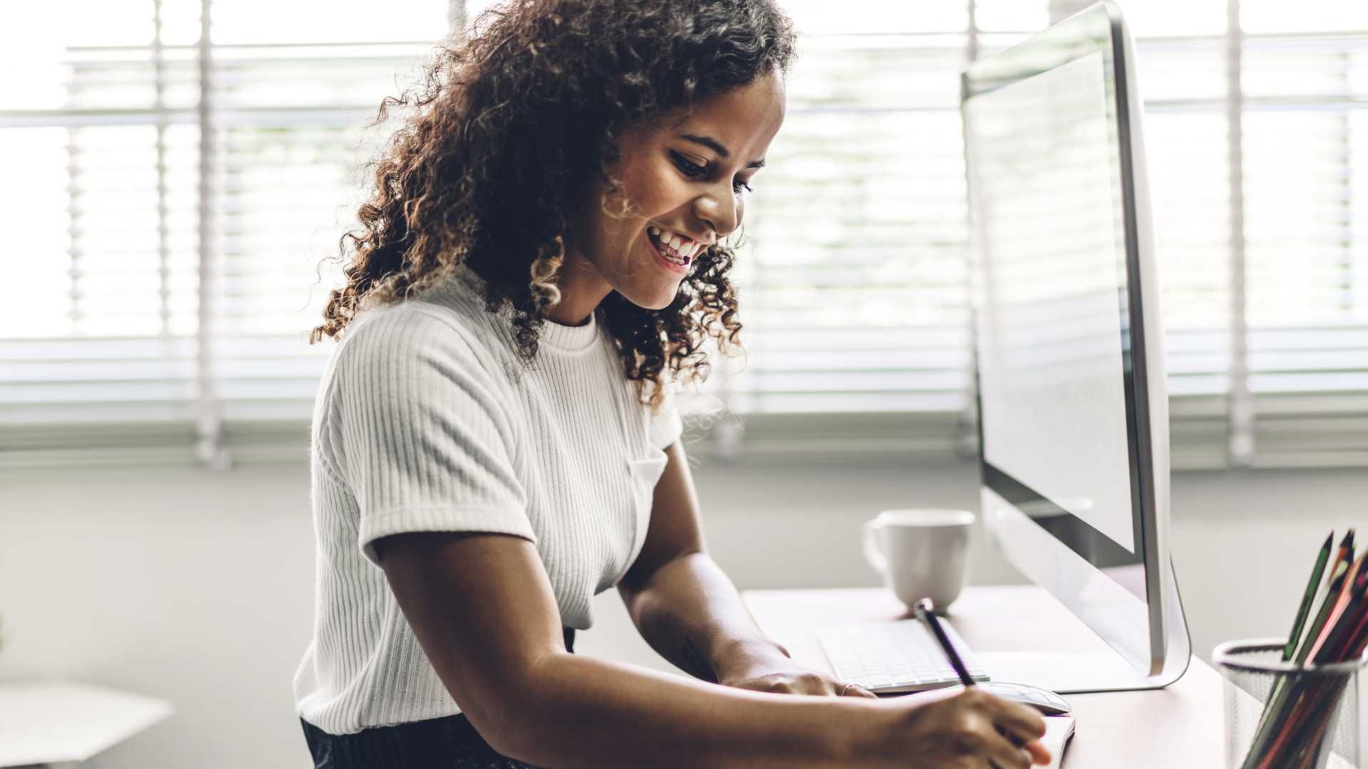 black woman on her computer writing down her appointment details on a piece of paper