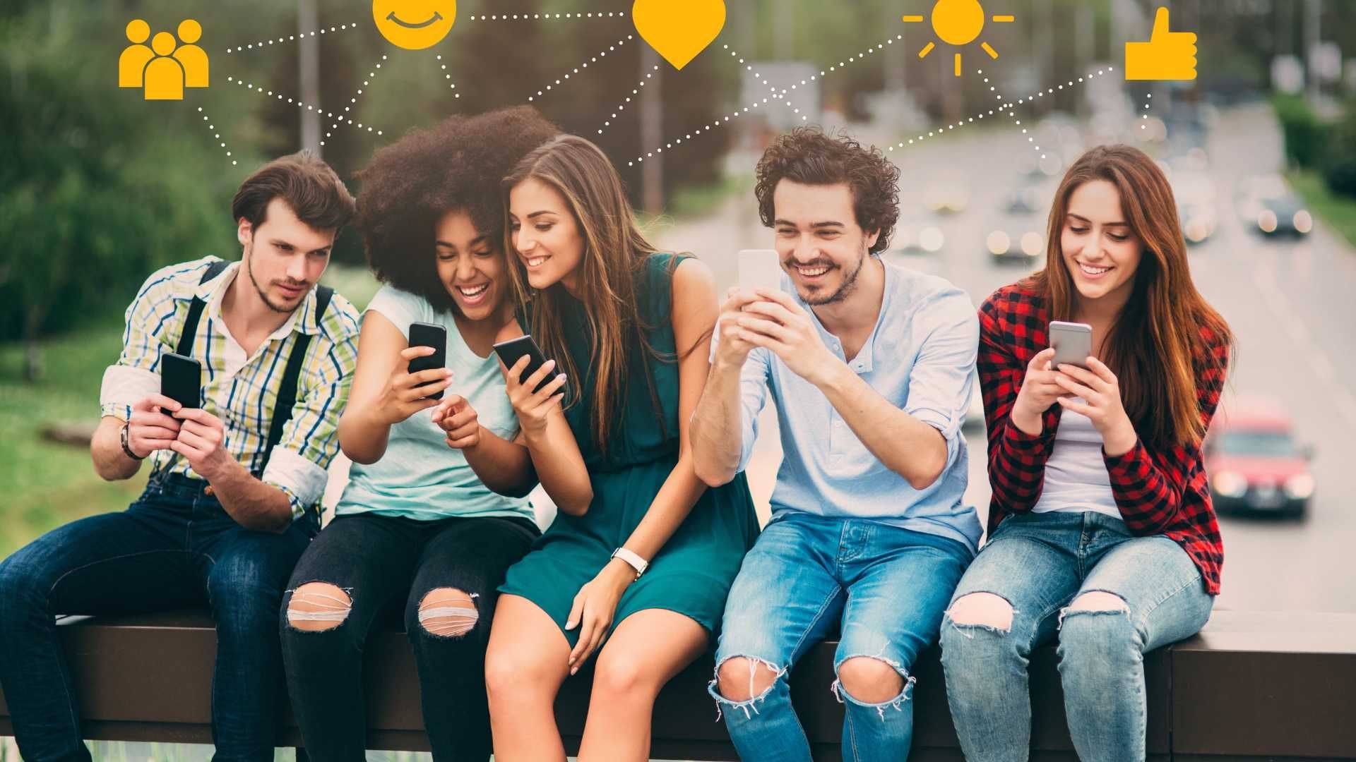 A group of young people are sitting on a railing looking at their phones.