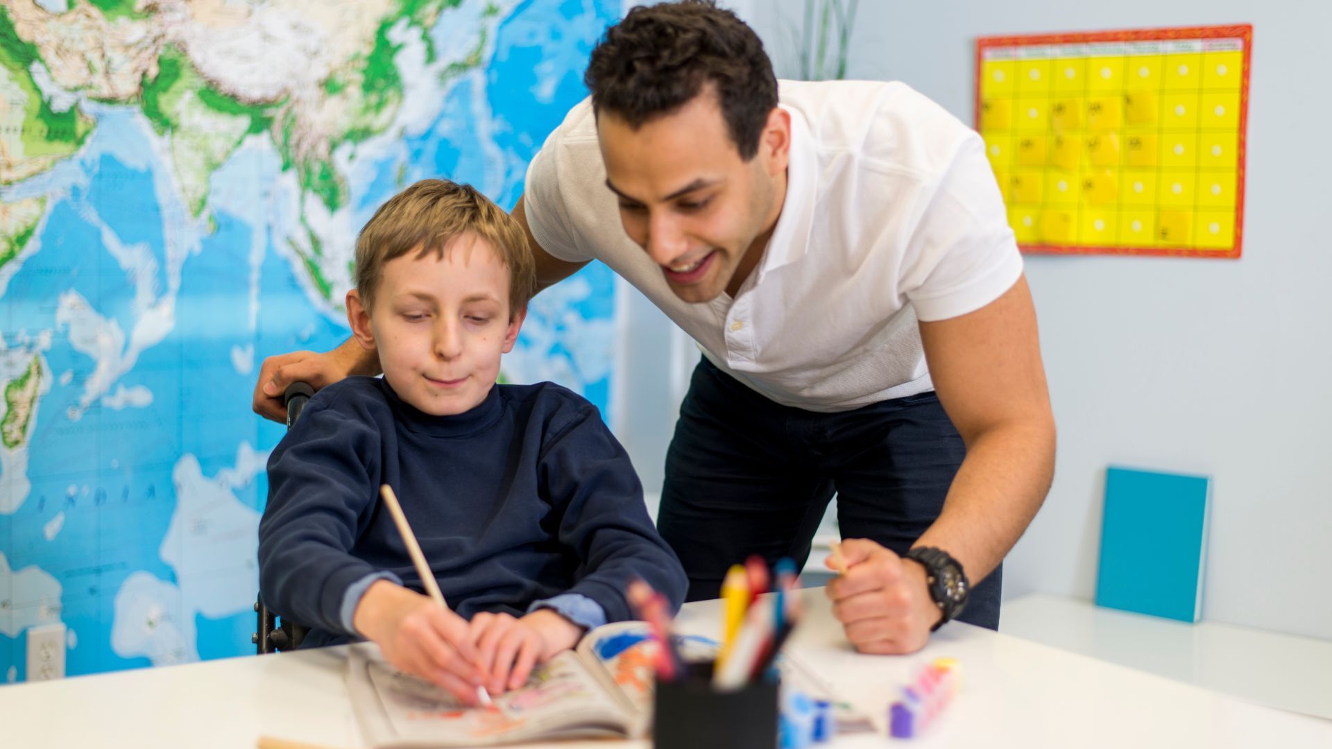 man bending down to watch what the child is writing on a peace of paper on the table