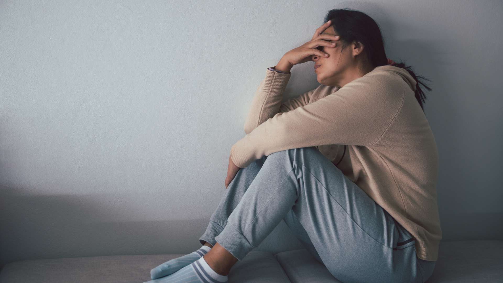 A woman is sitting on the floor covering her face with her hand.