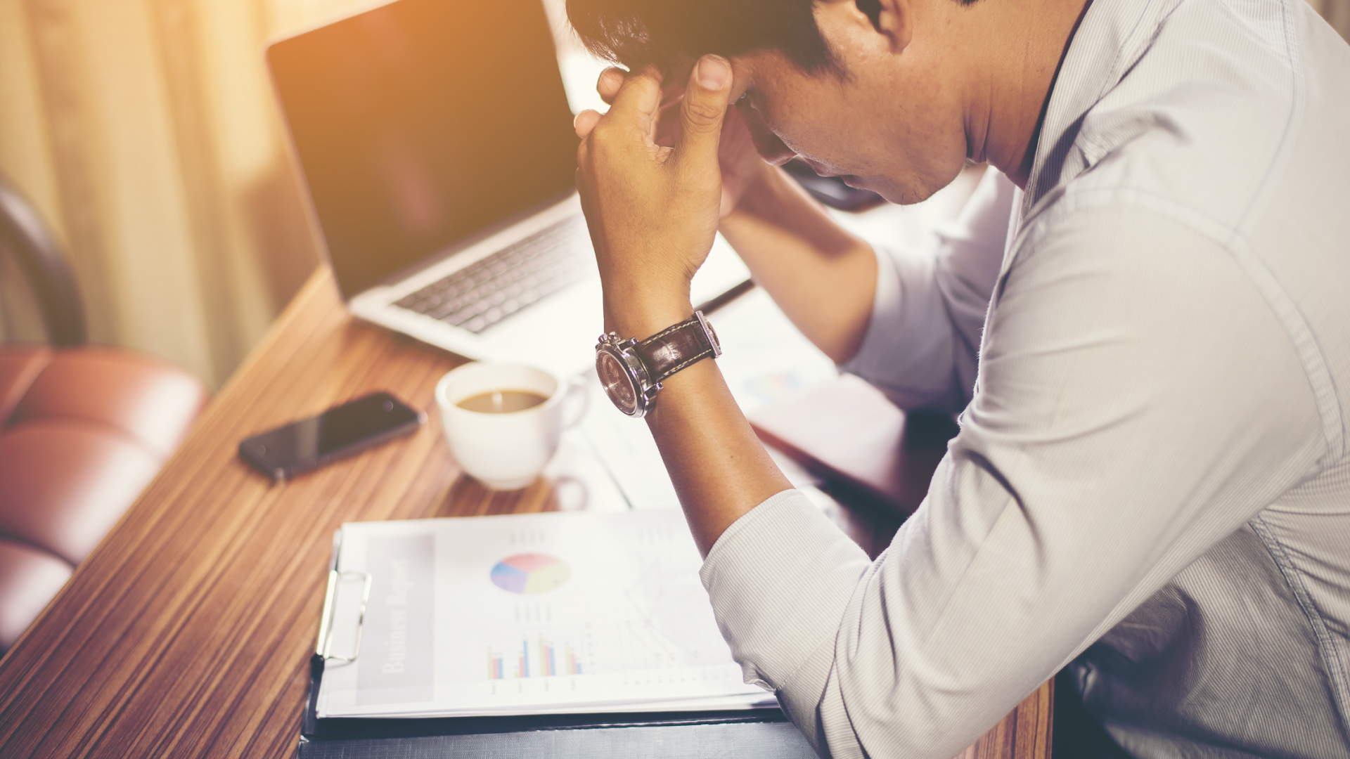 man on his work table facing down while touching his forehead with both of his hands looking worried
